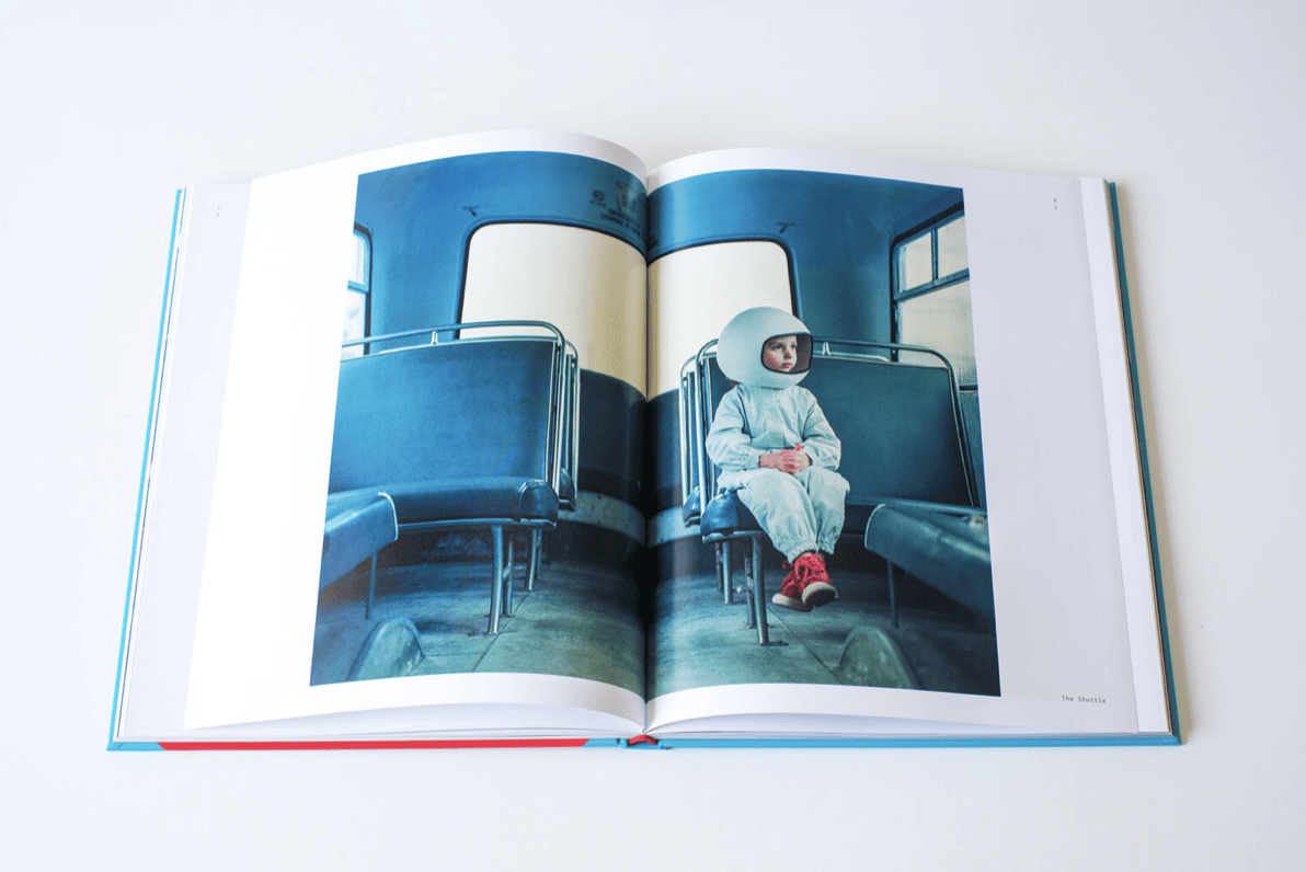 Una bambina con un casco da astronauta seduto su sedili blu di un veicolo, con scarpe rosse, in un'immagine tratta da un libro intitolato 'The Rocketgirl Chronicles'