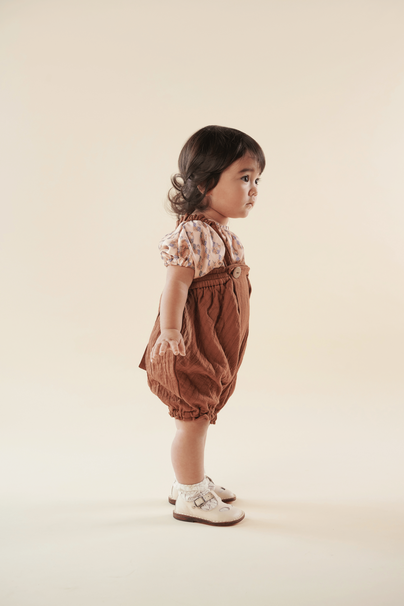cute japanese baby girl posing in terracotta romper and printed shirt