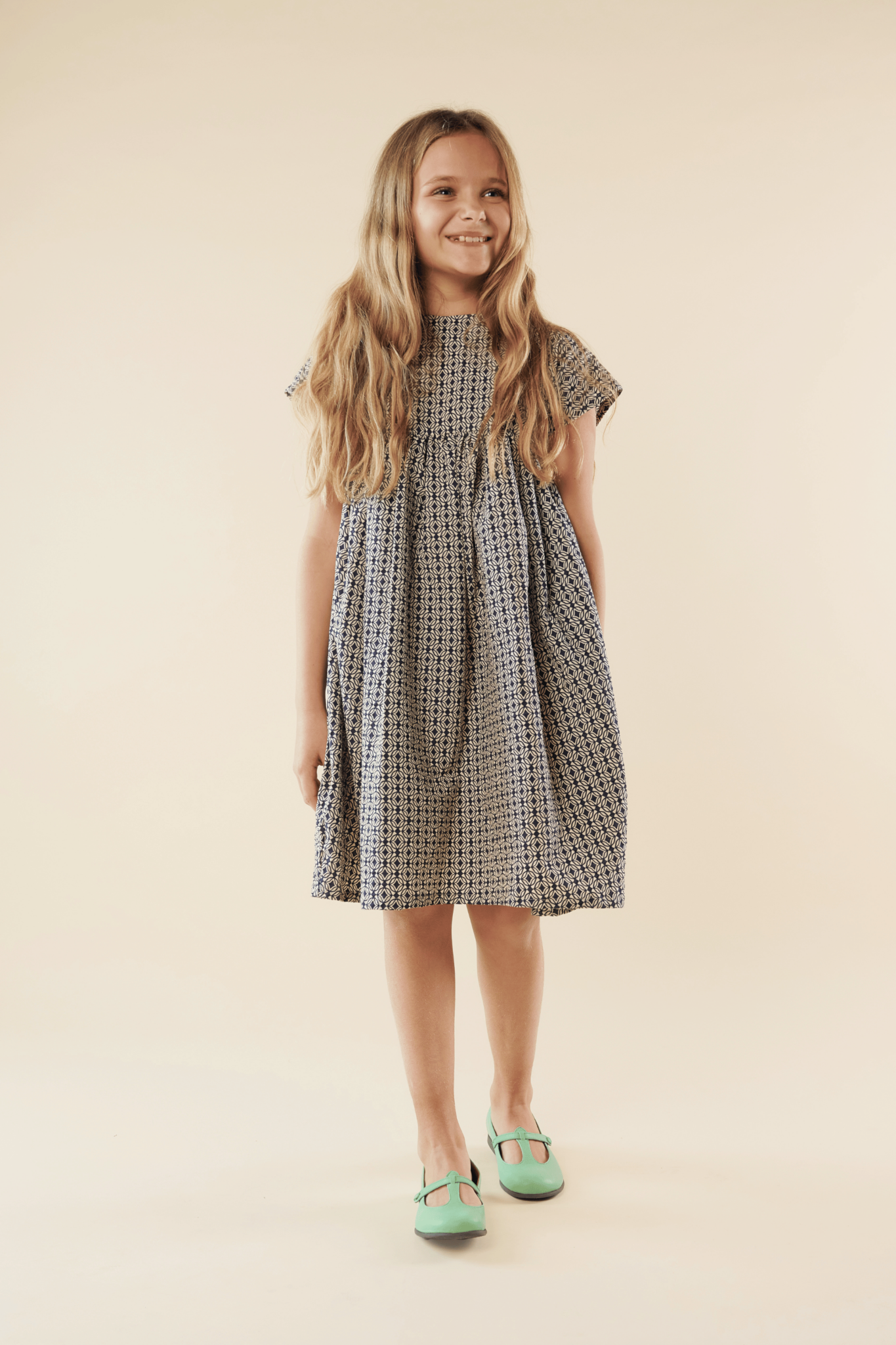 blonde girl with posing with patterned dress and green Mary Janes
