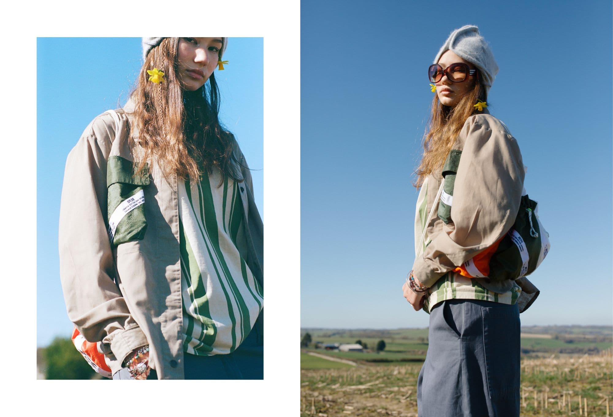 Girl standing in a field under a clear blue sky, wearing a green and beige color-blocked jacket with a green striped shirt underneath, wide-leg trousers, and a light blue wool hat. Yellow flowers are tucked behind her ears, and she carries a colorful drawstring backpack. One image shows her looking directly at the camera; the other captures a side view with oversized sunglasses.