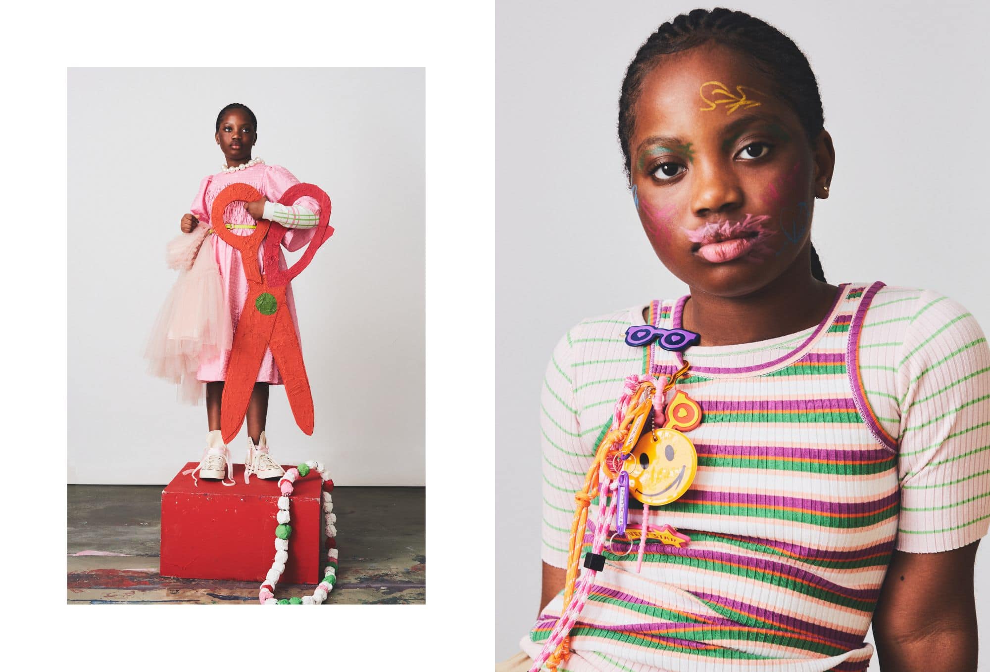 Creative children’s fashion editorial with a bold, expressive twist. On the left, a girl stands confidently on a red block, holding oversized red paper-mâché scissors. She wears a pink textured dress layered over a pastel checkered top, with cream tulle draped from one shoulder and white sneakers on her feet. A chunky paper bead necklace lays at her feet. On the right, a close-up reveals the same girl with vivid, hand-drawn face paint in colorful shapes and symbols. Her ribbed, striped top in green, pink, and cream tones is adorned with a cascade of playful accessories, including cartoonish charms, ropes, and smiley badges.
