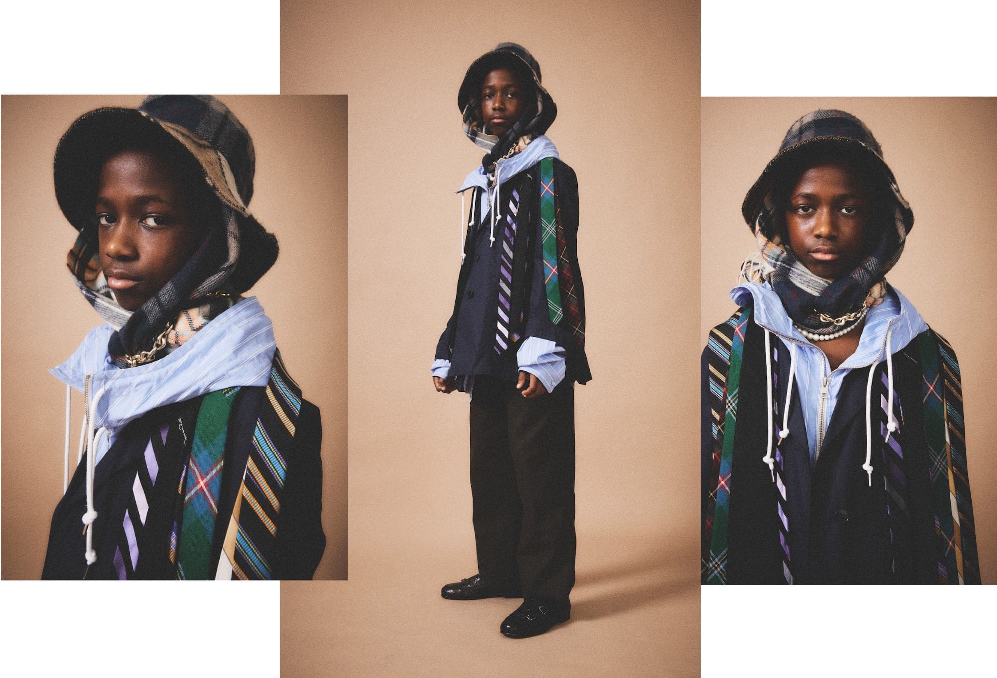 Fashion editorial by Molly Magnuson featuring a young model in layered, eclectic styling. The model wears a patchwork flannel bucket hat with scarf wrapped underneath, a blue pinstripe hoodie over a blazer, and multiple neckties in contrasting patterns draped over the shoulders. The outfit is accessorized with a chunky chain necklace and wide-leg dark trousers. Captured against a beige background, the look combines preppy, streetwear, and avant-garde influences with a playful, textural twist.