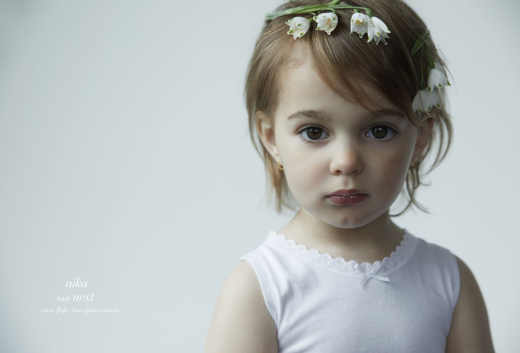 Ritratto ravvicinato di bambina piccola con top bianco e coroncina di piccoli fiori campanella bianchi tra i capelli; editoriale moda “Moon Garden” di Cleo Sullivan.