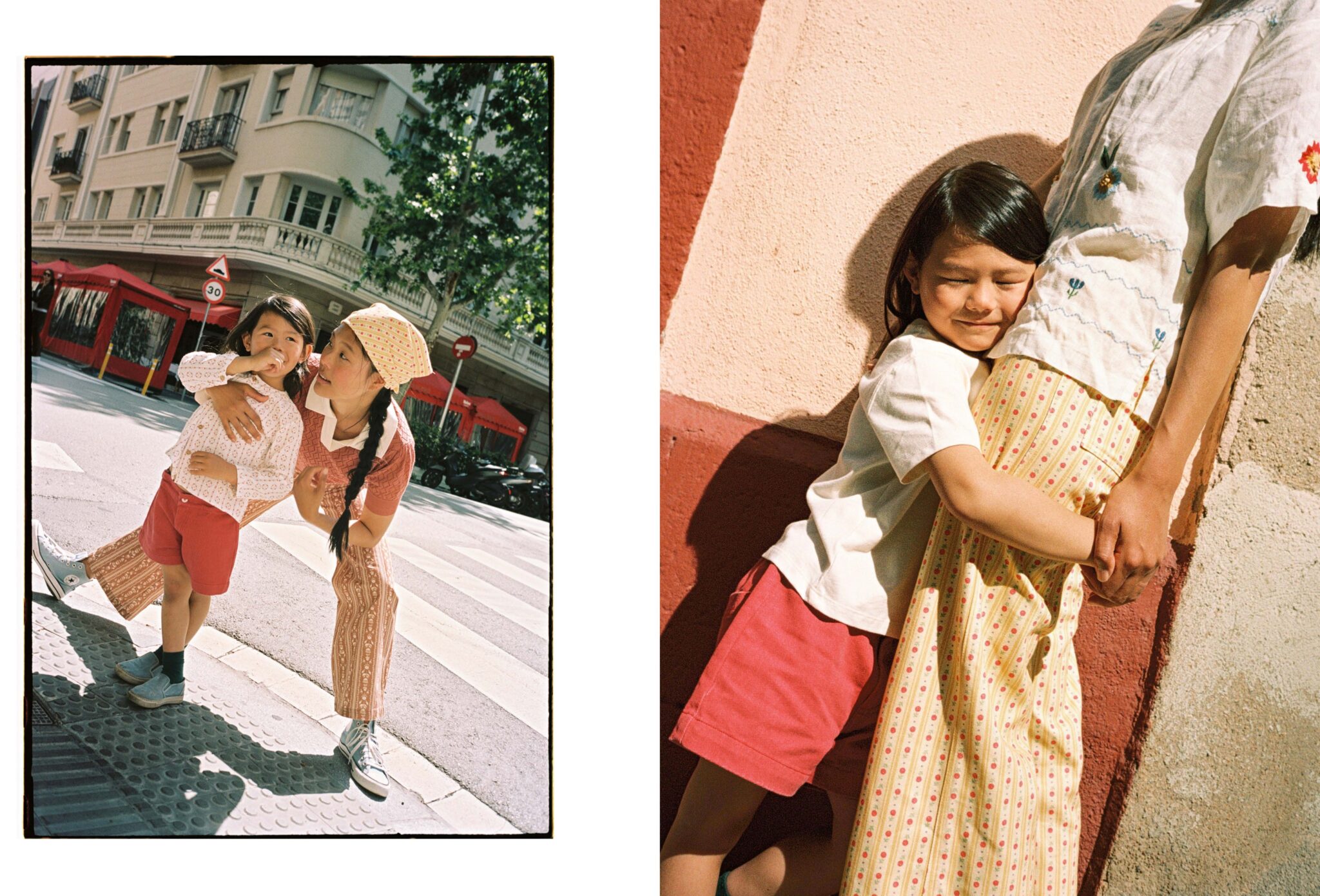 Two vibrant street-style portraits by Paola Amenta. On the left, a playful moment between mother and daughter as they lean toward the camera on a city crosswalk, both smiling and full of energy. On the right, the little girl hugs her mother’s legs tightly, eyes closed in a gesture of affection and security, both bathed in warm sunlight against a red and cream wall.