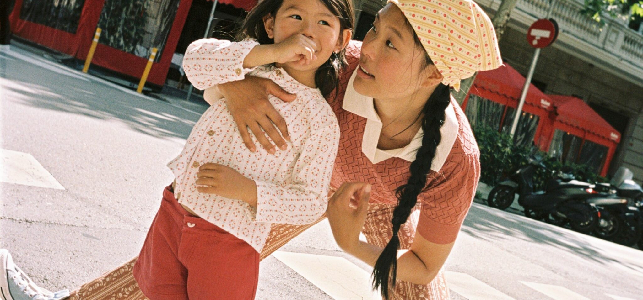a playful moment between mother and daughter as they lean toward the camera on a city crosswalk, both smiling and full of energy.