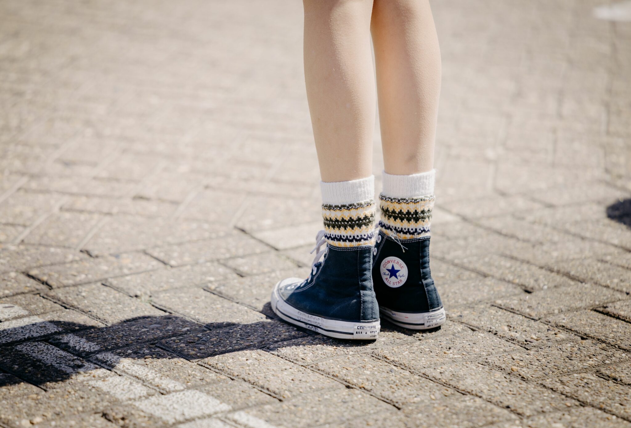 Close-up of a teen girl’s legs wearing patterned knit socks and worn navy Converse All Star high-top sneakers, part of Amsterdam Beach fashion editorial for Scimparello Magazine SS25, photographed by Arjaan Hamel.