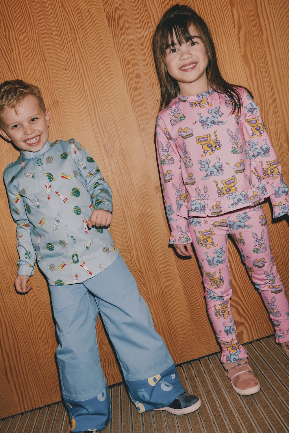 Småfolk F/W25 – kidswear fall winter 2025, boy in rocket print shirt and wide pants, girl in pink pajama with robot animals.