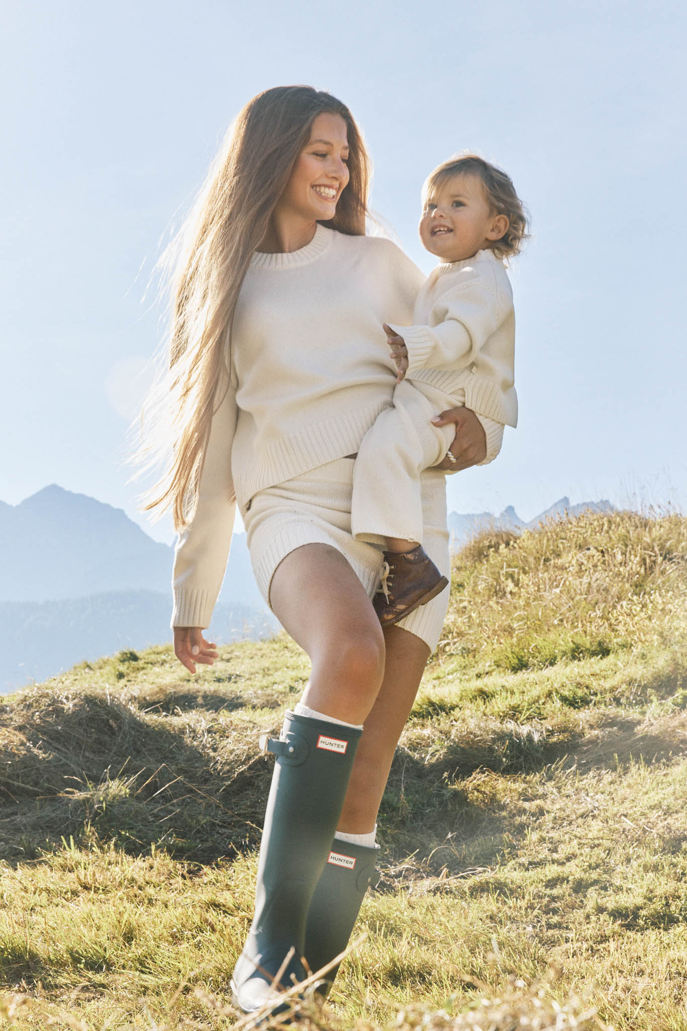 Mother and child in coordinated cream knit outfits from the Minimalisma x Zoë Pastelle capsule collection Fall/Winter 25, featured on Scimparello Magazine, styled outdoors in the mountains.
