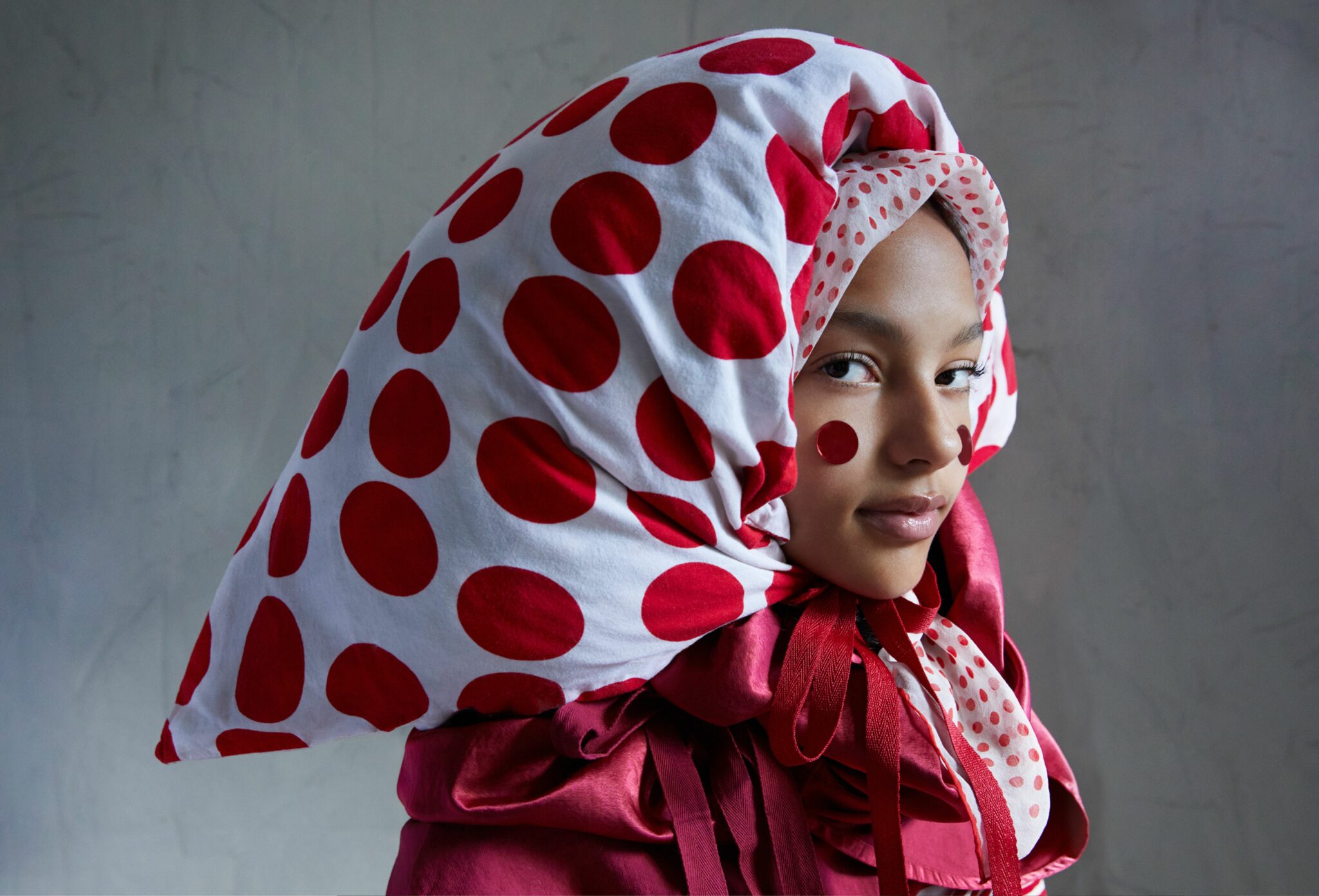 Fashion editorial That’s Bonkers for Scimparello Magazine FW25, photographed by Cleo Sullivan. A girl in a voluminous red outfit with an oversized polka-dot headpiece made from custom-made NEW YORK ELEGANT FABRICS, layered scarves VINTAGE HUDSON NY, and a vintage MAISON MARGIELA skirt. The playful red-and-white palette and sculptural styling create a surreal, avant-garde mood.