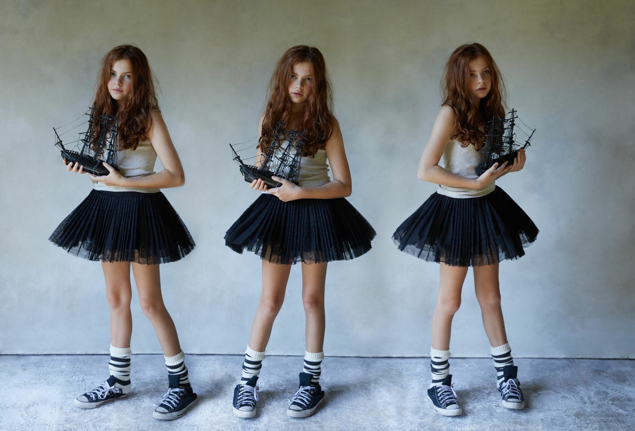 Fashion editorial That’s Bonkers for Scimparello Magazine FW25, photographed by Cleo Sullivan. Three mirrored images of a red-haired girl holding a black model ship, wearing a tank top RALPH LAUREN FW25, black tutu BLOCH FW25, striped socks MOSHI MOSHI MIND FW25, and sneakers CONVERSE FW25. The repetition and nautical prop create a playful, surreal rhythm with a touch of rebellion.