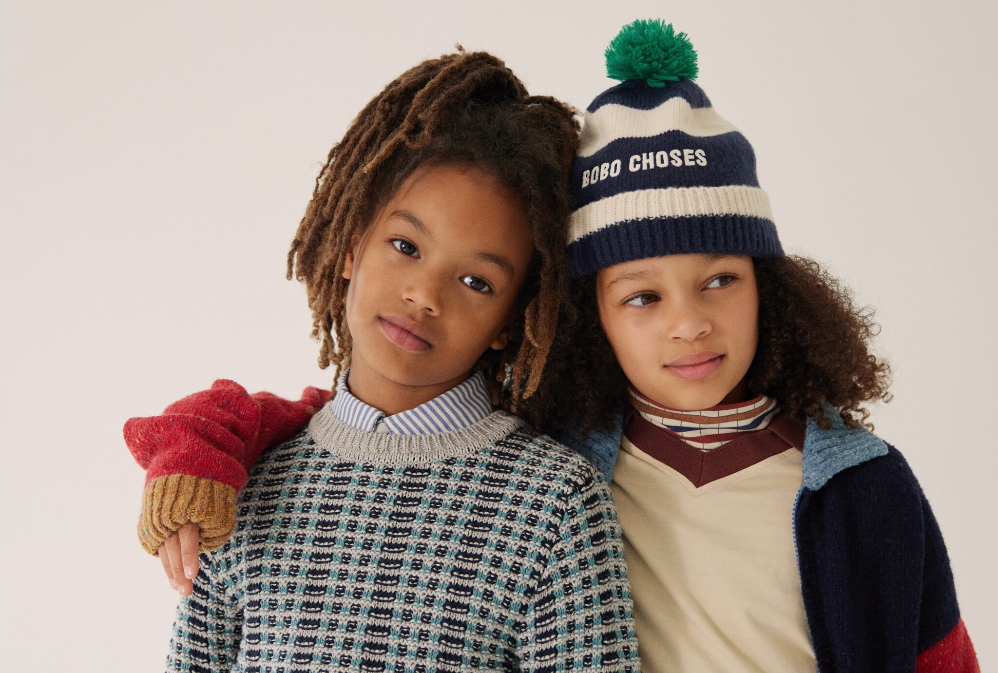 Two children posing together from Dancing With Myself FW25 by Alex Klever for Scimparello Magazine. Left: wearing shirt KENZO and pullover BEBE ORGANIC. Right: wearing cardigan and hat BOBO CHOSES, turtleneck COCO AU LAIT, and longsleeve MAIN STORY. A cozy and modern kidswear look celebrating friendship and individuality.