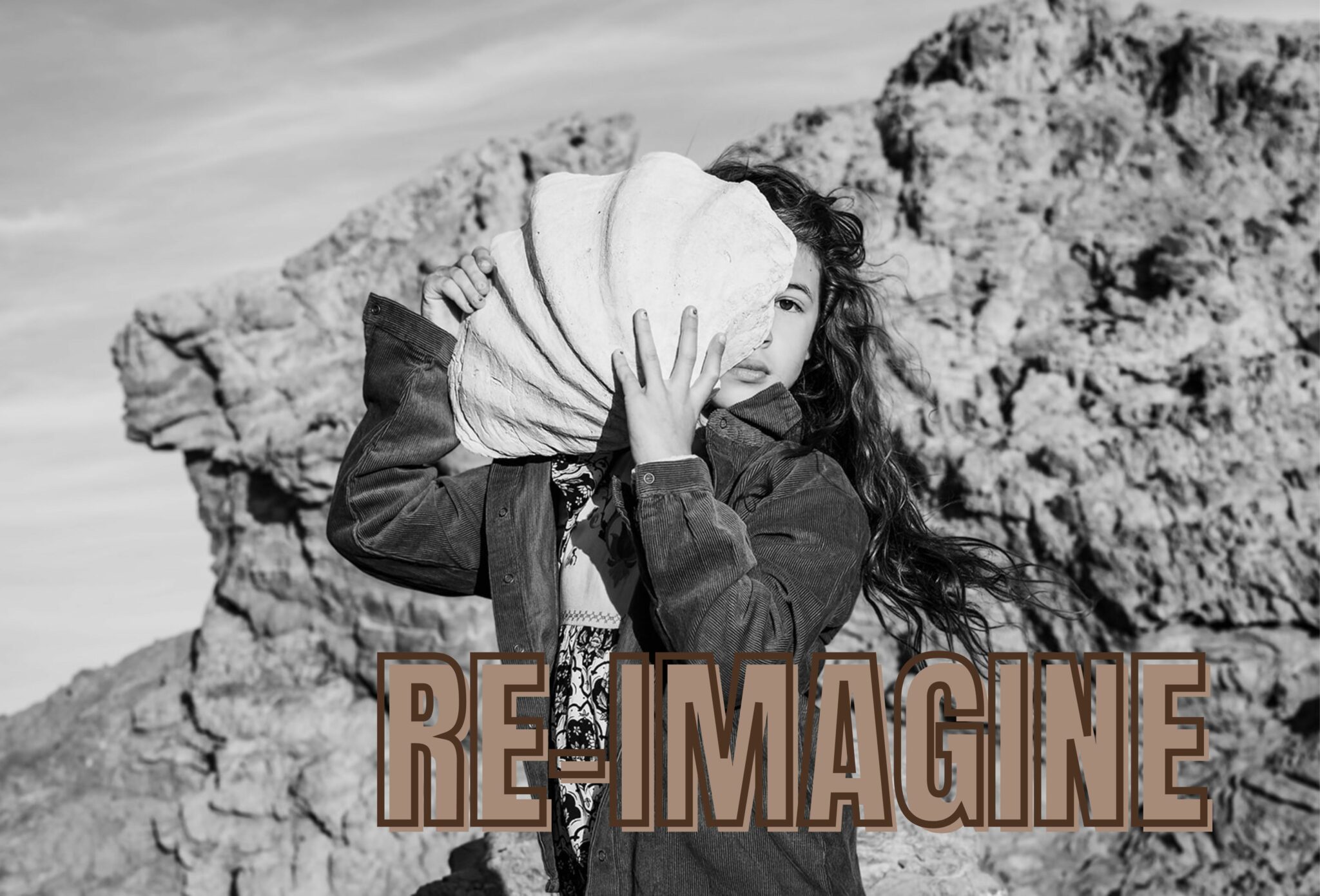 Girl holding a large shell in front of her face in a rocky landscape, photographed by Manuela Franjou for Scimparello Magazine.