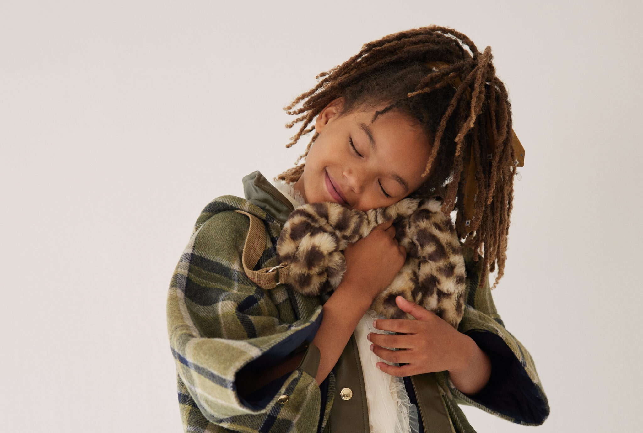 Girl hugging a furry bag with a smile, wearing coat/poncho CHLOÉ, blouse C’ERA UNA VOLTA, bag BELLEROSE, and vintage bow. From Dancing With Myself FW25 by Alex Klever for Scimparello Magazine – a tender, heartwarming moment celebrating softness and self-love in kids’ fashion.