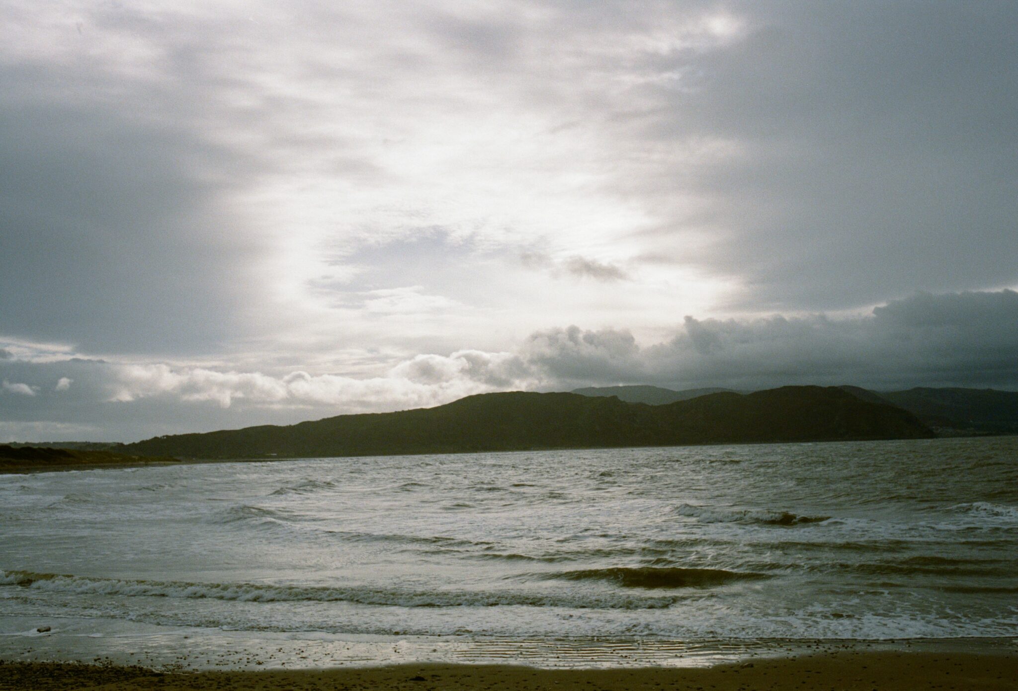 Coastal landscape with sea waves and distant hills under a dramatic cloudy sky, photographed by Hannah Mentz for the kids fashion editorial Elemental in Scimparello Magazine.