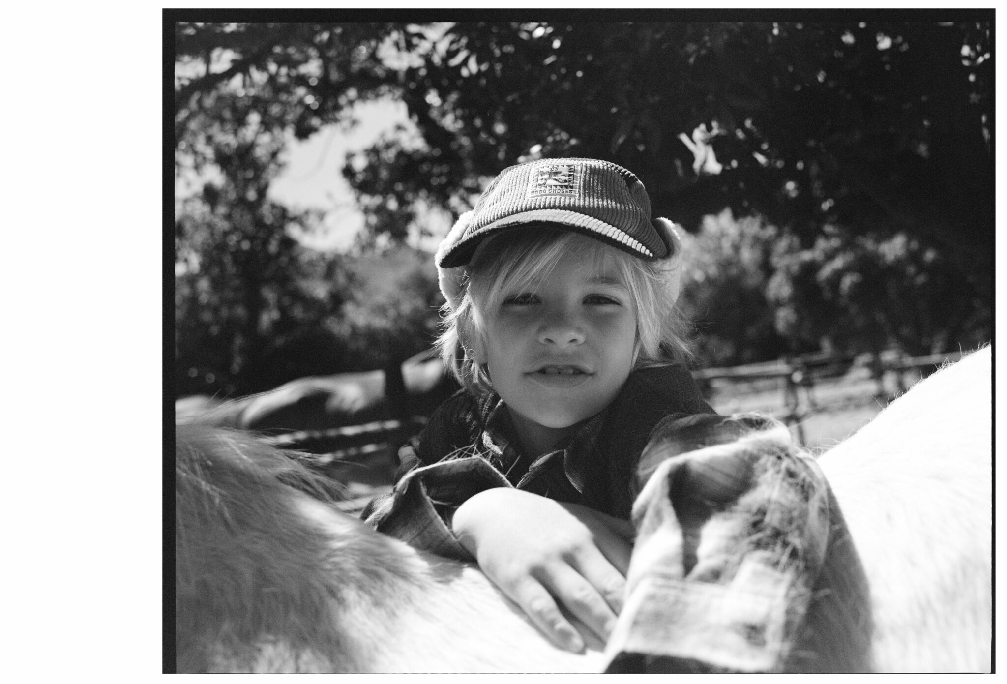 Black and white portrait of a child leaning on a pony, wearing a cap and layered countryside look in the kids fashion editorial Mosi. Photo by Alessandro Iovino, styling by Ulrike Kache, for Scimparello Magazine.
