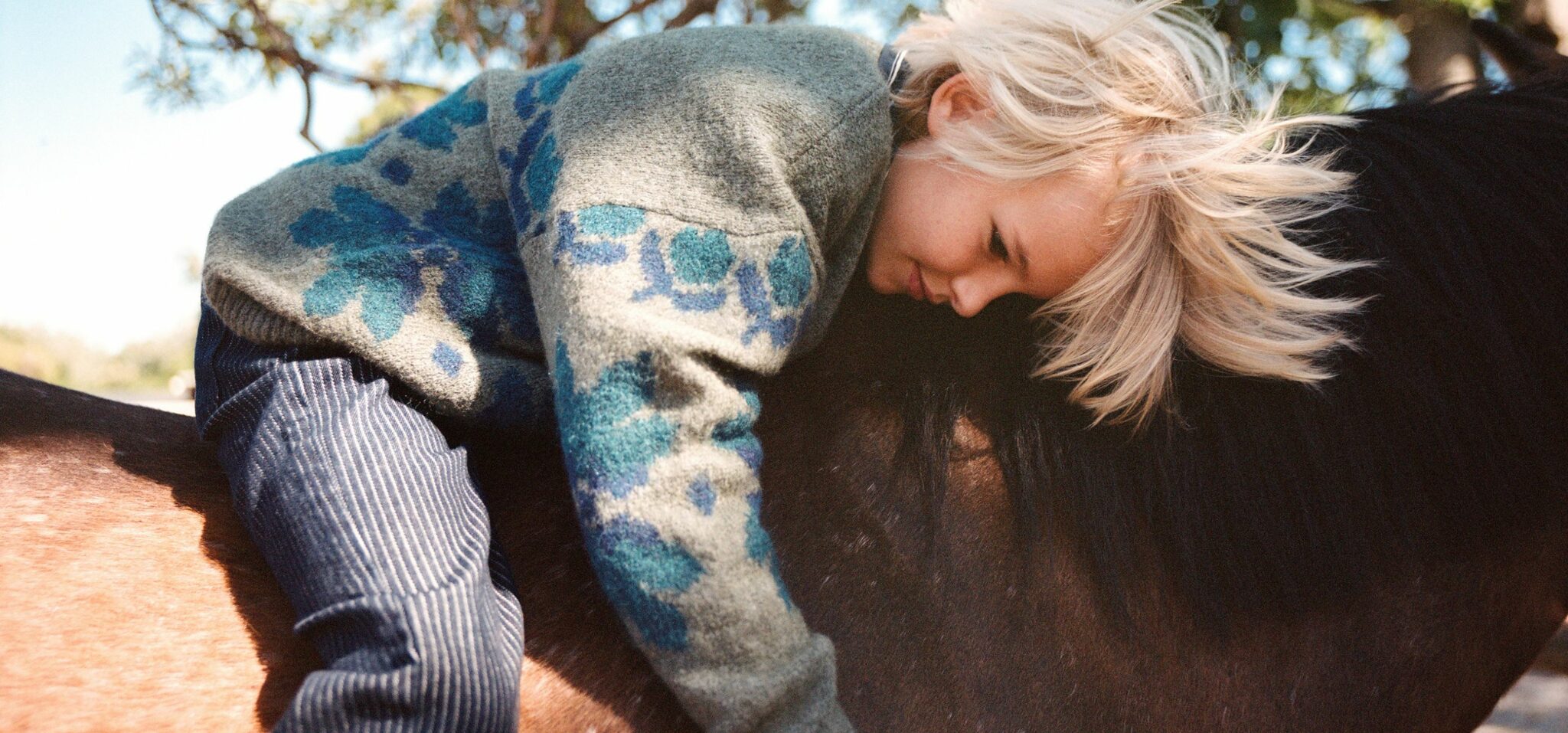 Child lying gently across a pony’s back in a quiet outdoor setting, wearing a patterned knit and striped trousers for the kids fashion editorial Mosi. Photo by Alessandro Iovino, styling by Ulrike Kache, for Scimparello Magazine.