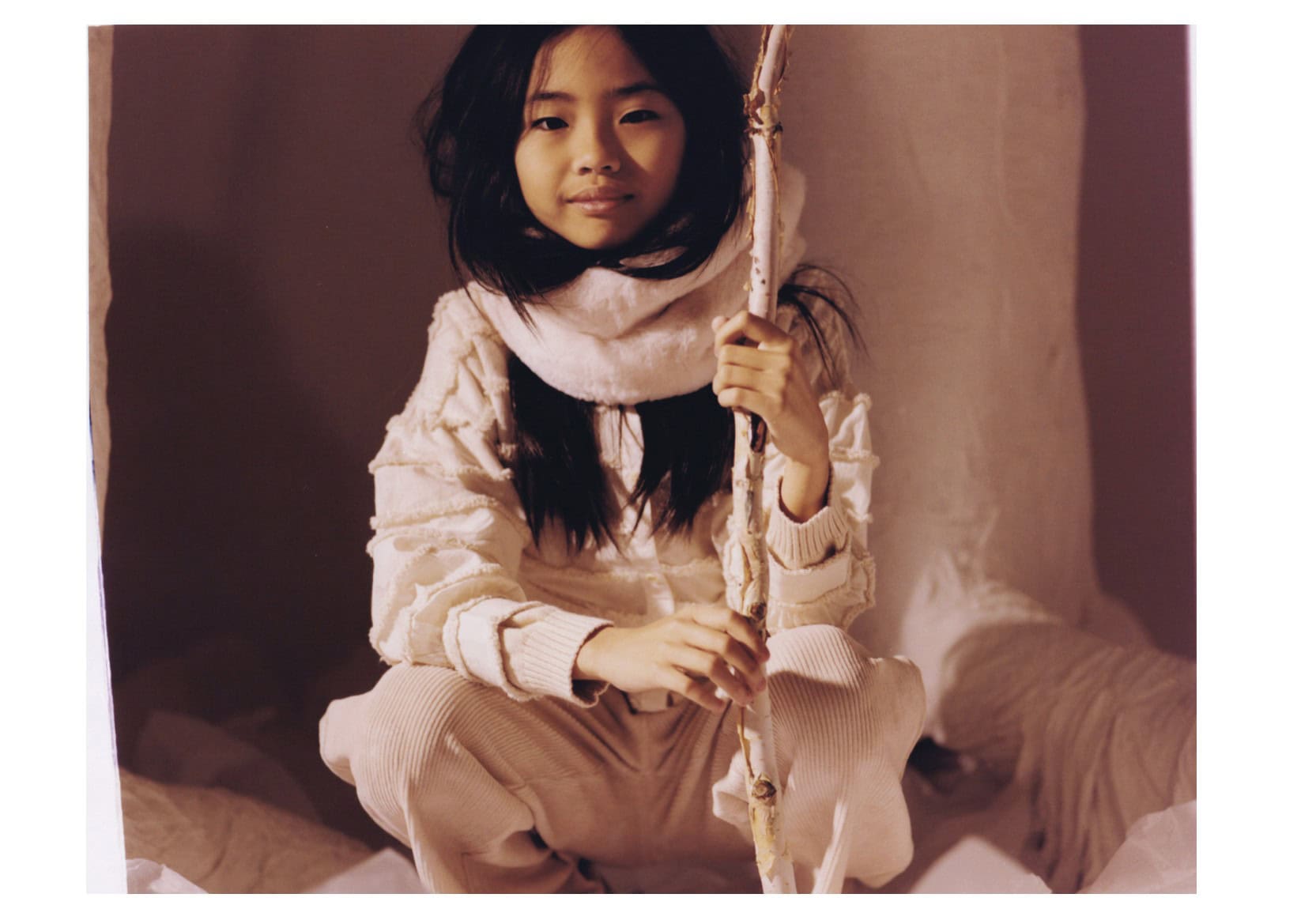 Girl sitting in soft layered winter textures, holding a wooden stick; editorial Wild Within for Scimparello Magazine, FW25. Photo by Emma Wright, styling by Holly Moluluo.