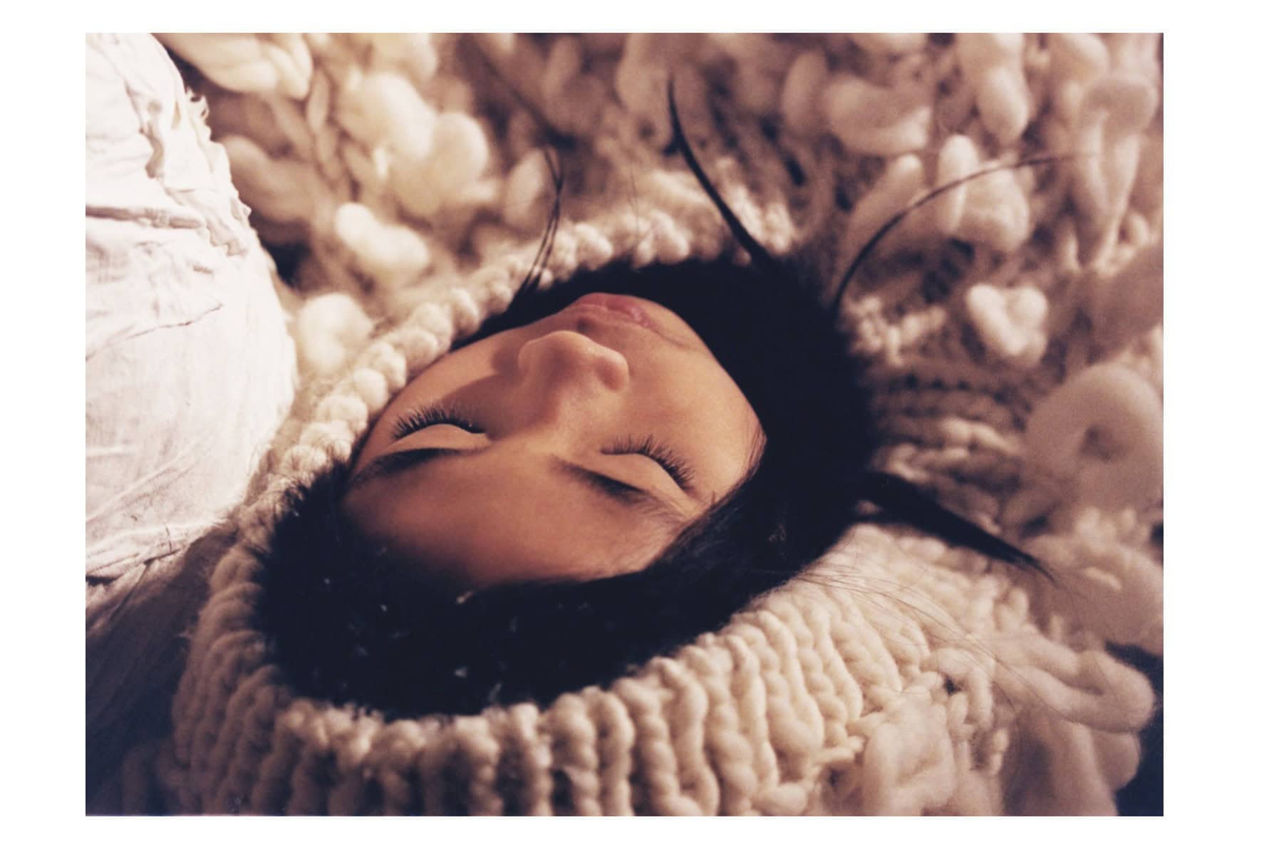 Close-up of a girl resting with eyes closed, wrapped in thick sculptural white knitwear; editorial Wild Within for Scimparello Magazine, FW25. Photo by Emma Wright, styling by Holly Moluluo.