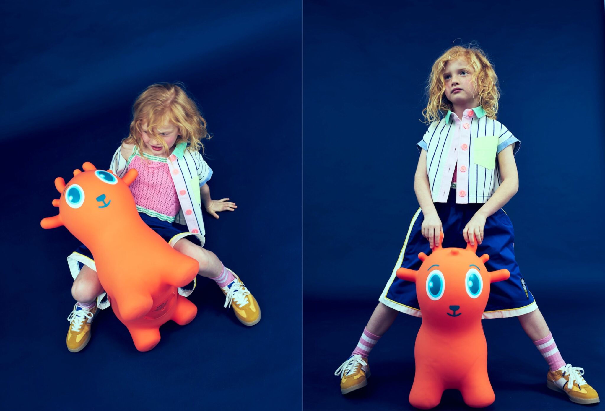 Kids fashion editorial Funky Monkey for Scimparello Magazine featuring a red-haired child in a deep blue studio setting, wearing a striped short-sleeve shirt with pastel pocket, pink knit top, wide navy skirt with yellow trim, pink striped socks and mustard sneakers, posing with a bright orange inflatable animal toy. Photo by Valerie Mathilde.