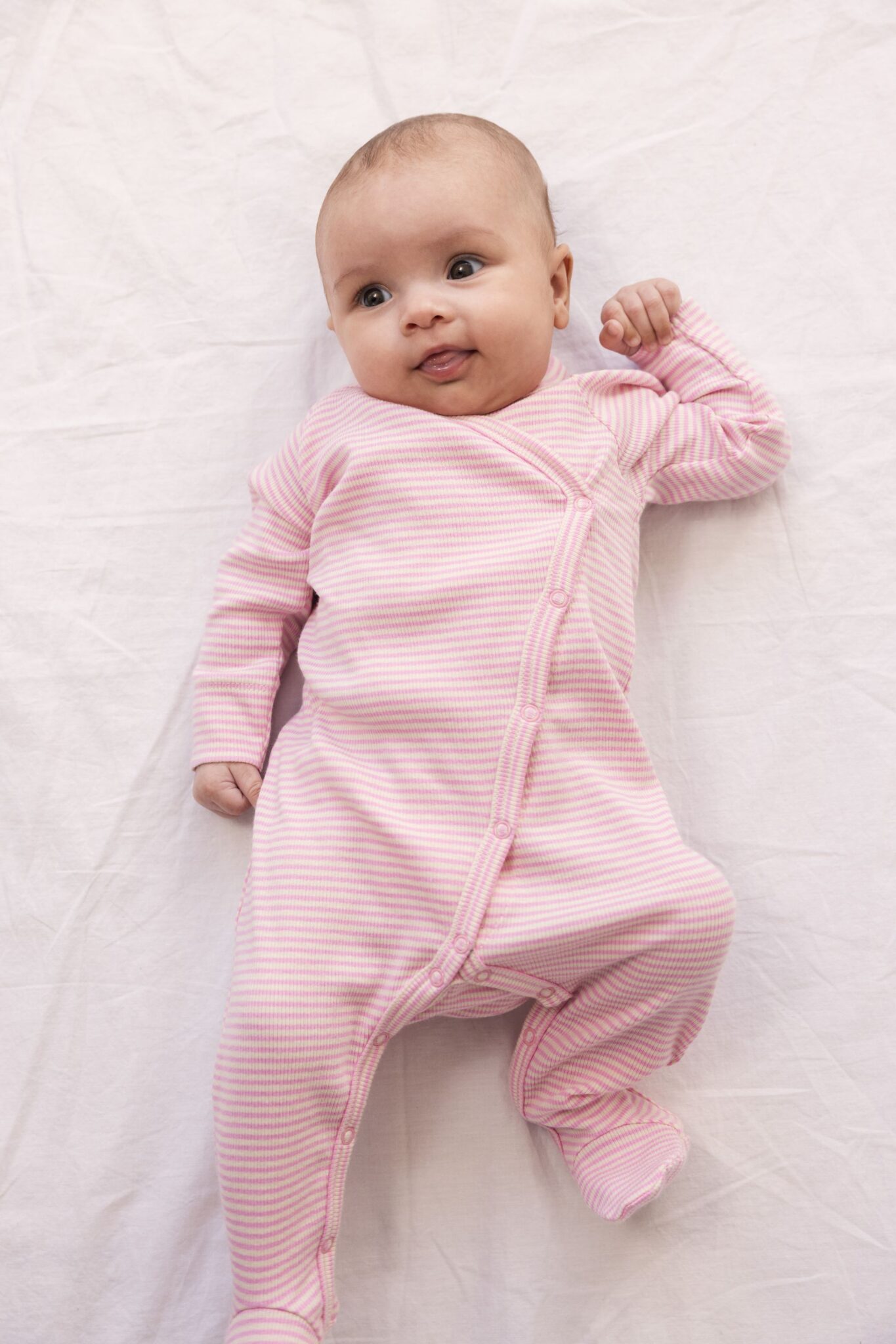 MarMar Copenhagen SS26 baby collection featured in Scimparello Magazine – baby lying on a soft white sheet wearing a pink and white striped long-sleeve romper with snap buttons, gentle natural light and minimal background.
