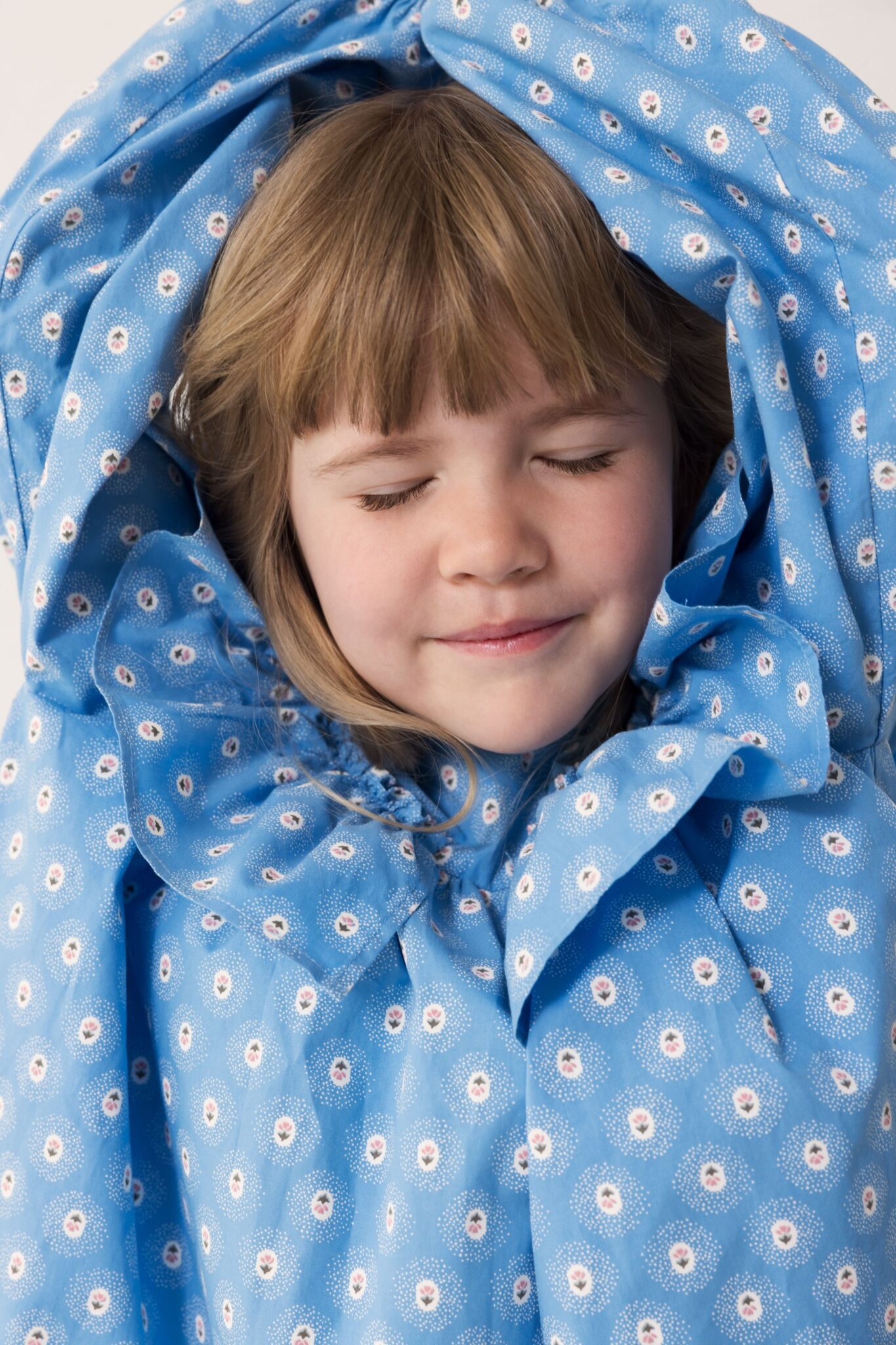 MarMar Copenhagen SS26 kids collection featured in Scimparello Magazine – close-up portrait of a child with eyes closed wrapped in a blue floral printed fabric, soft light and delicate small flower pattern.
