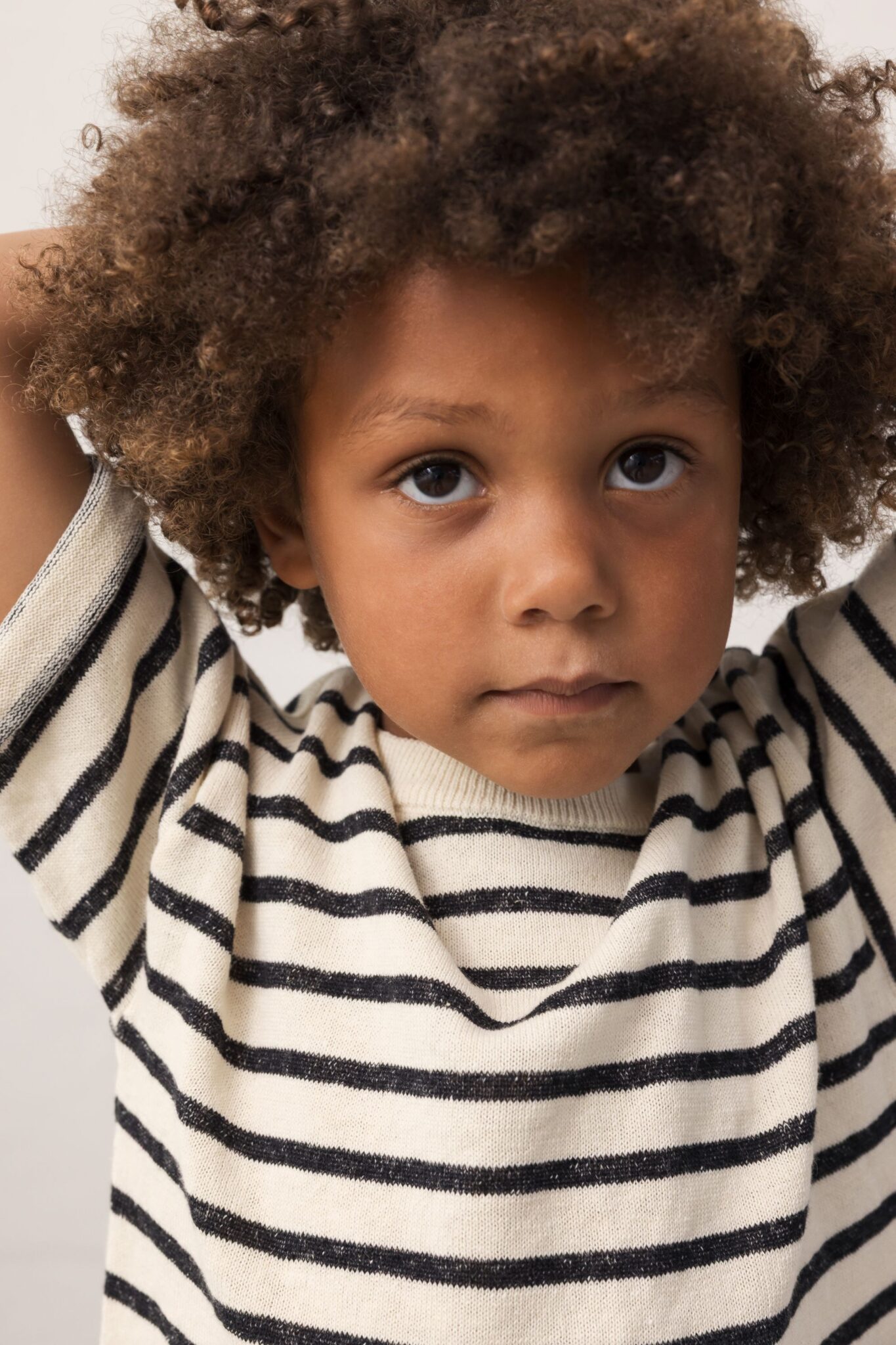 MarMar Copenhagen SS26 kids knitwear featured in Scimparello Magazine – close-up of a child with curly hair wearing a cream and navy striped sweater, neutral studio background and natural tones.