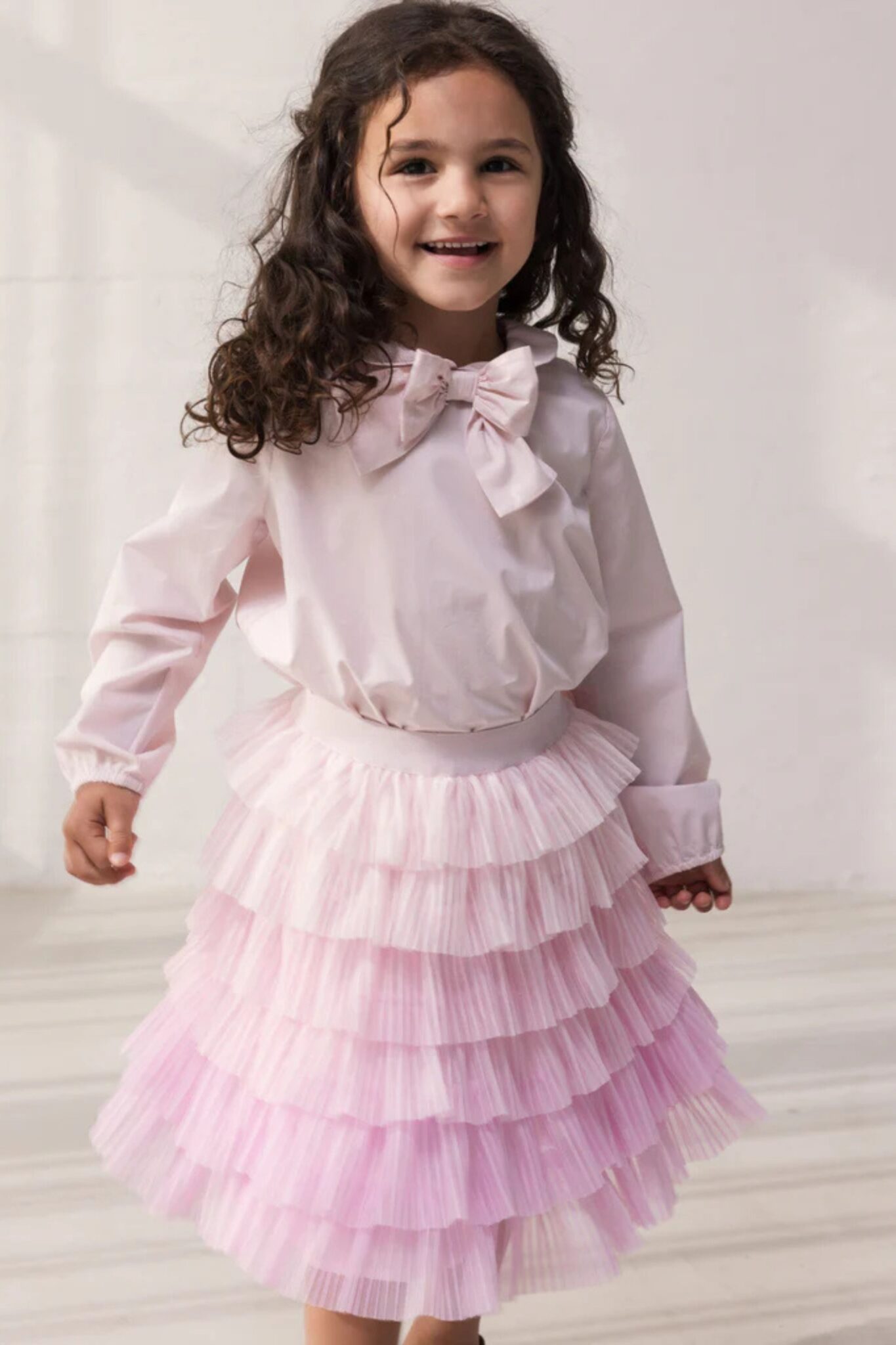 MarMar Copenhagen SS26 girls collection featured in Scimparello Magazine – smiling girl in a pale pink blouse with bow detail paired with a layered pink tulle skirt, photographed in natural studio light.