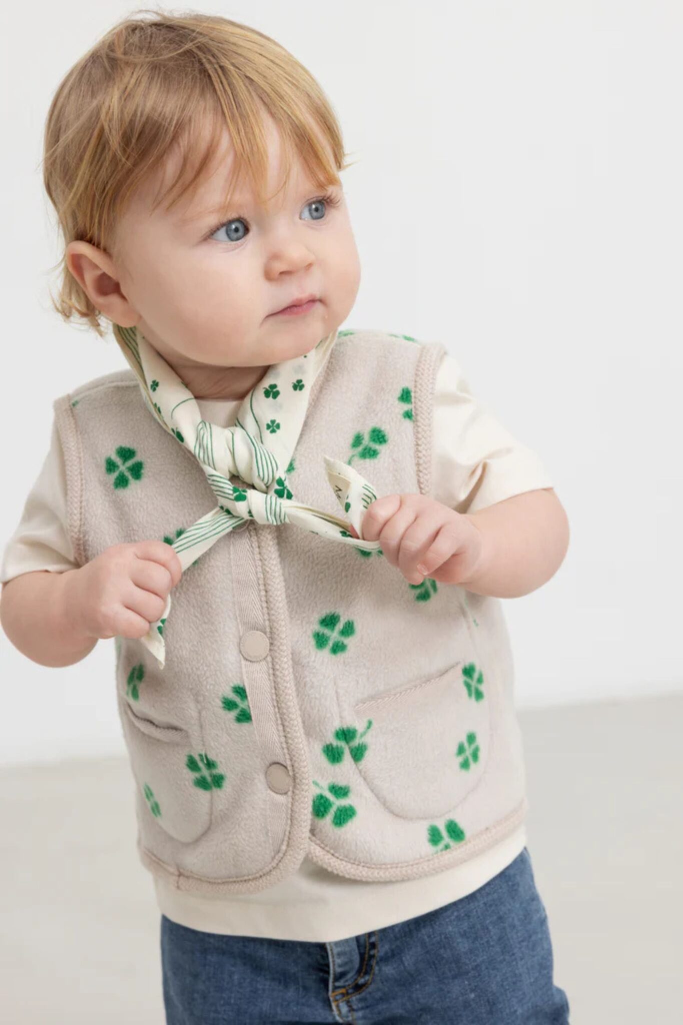 MarMar Copenhagen SS26 baby collection featured in Scimparello Magazine – toddler wearing a beige vest with green clover print over a cream T-shirt, styled with a printed neck scarf and denim trousers.