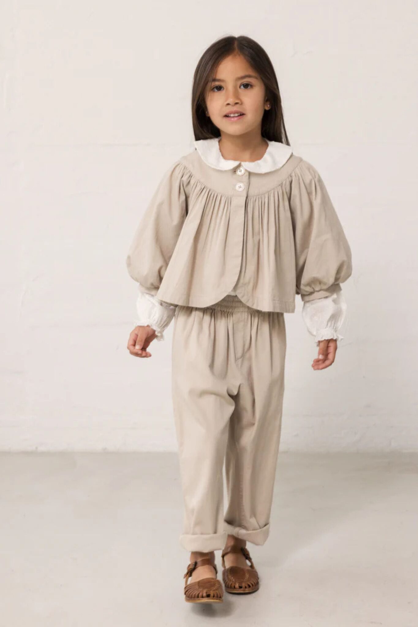 MarMar Copenhagen SS26 girls collection featured in Scimparello Magazine – girl in a beige two-piece set with puffed sleeves and white collar detail, paired with brown leather shoes in a neutral studio.
