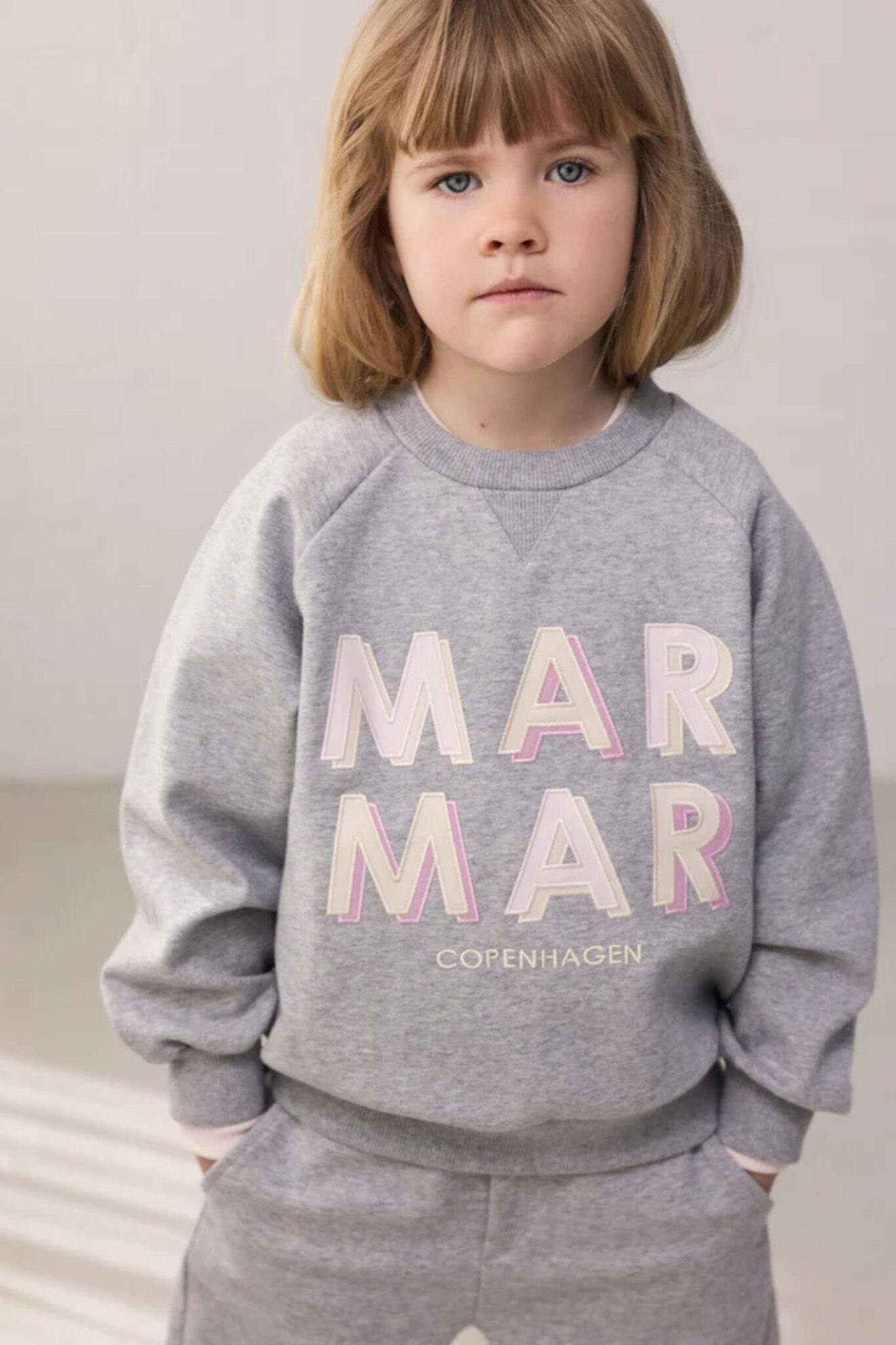 MarMar Copenhagen SS26 kids collection featured in Scimparello Magazine – child in a grey tracksuit with MAR MAR Copenhagen logo print, styled in a minimal studio environment.