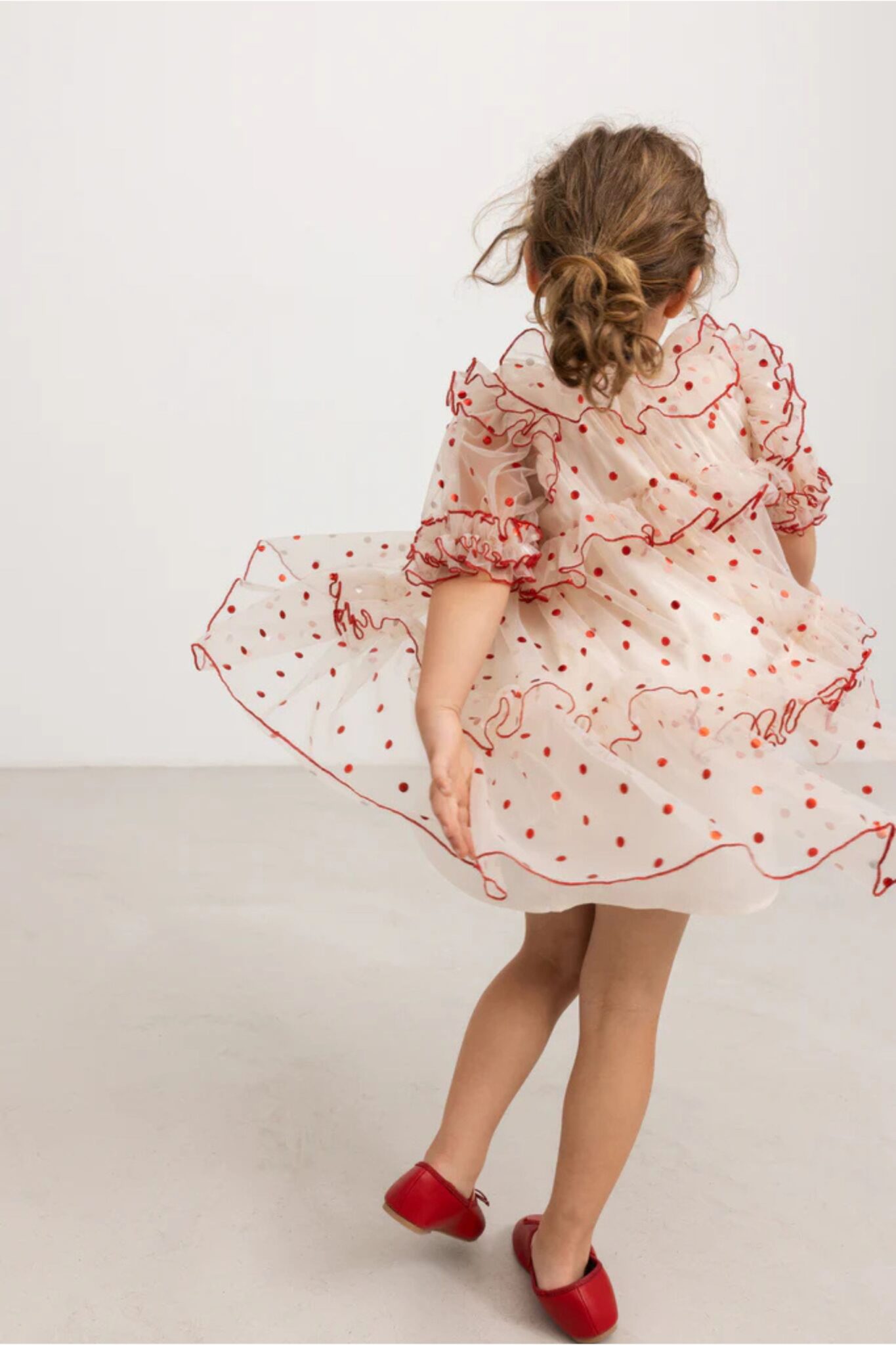 MarMar Copenhagen SS26 girls collection featured in Scimparello Magazine – girl twirling in a sheer cream dress with red polka dots and red trim details, paired with red shoes.