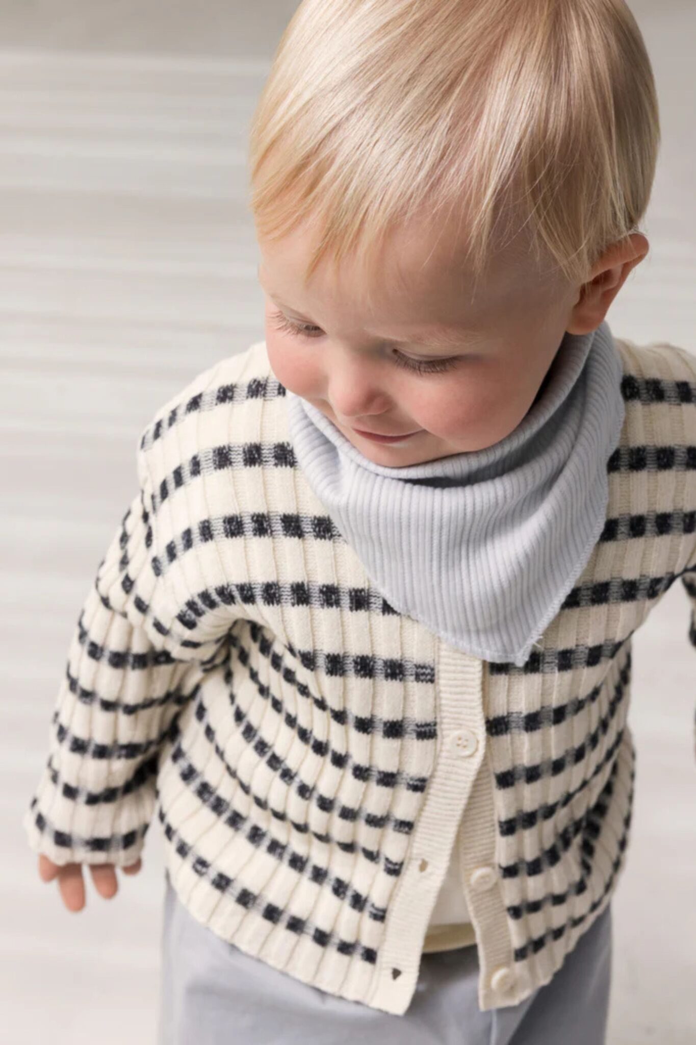 MarMar Copenhagen SS26 baby knitwear featured in Scimparello Magazine – close-up of baby in a cream and navy striped cardigan with a light grey bib scarf, soft neutral background.