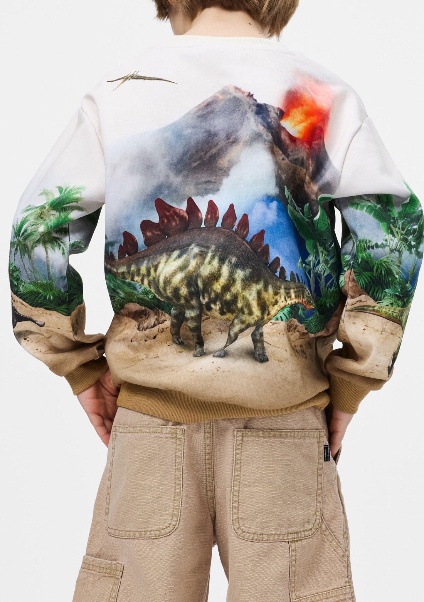 Boy wearing sweatshirt with stegosaurus print and erupting volcano graphic from Molo SS26, adventurous dinosaur kids fashion featured in Scimparello Magazine.