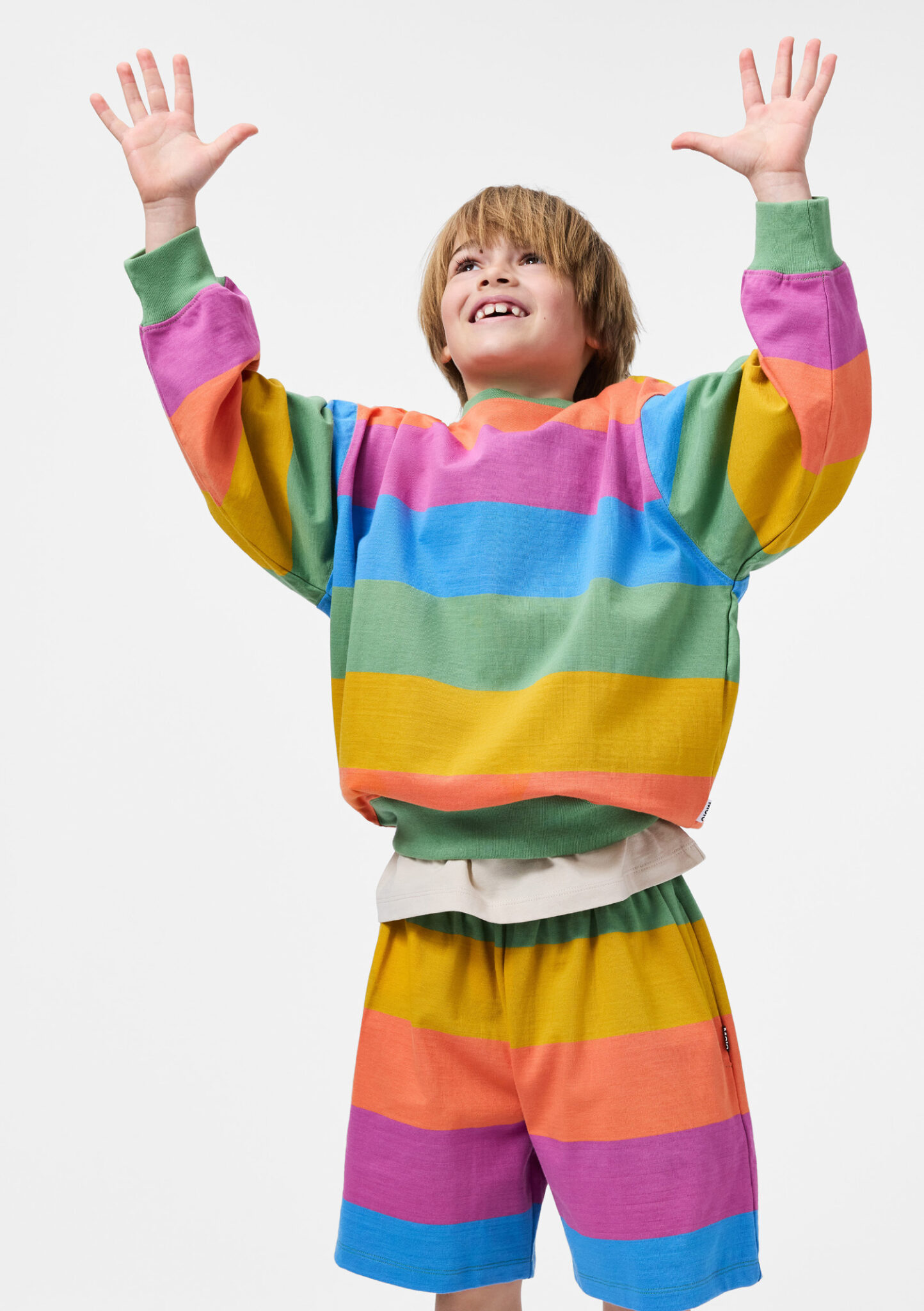 Boy wearing colorful striped sweatshirt and shorts set from Molo SS26, rainbow summer kidswear featured in Scimparello Magazine.