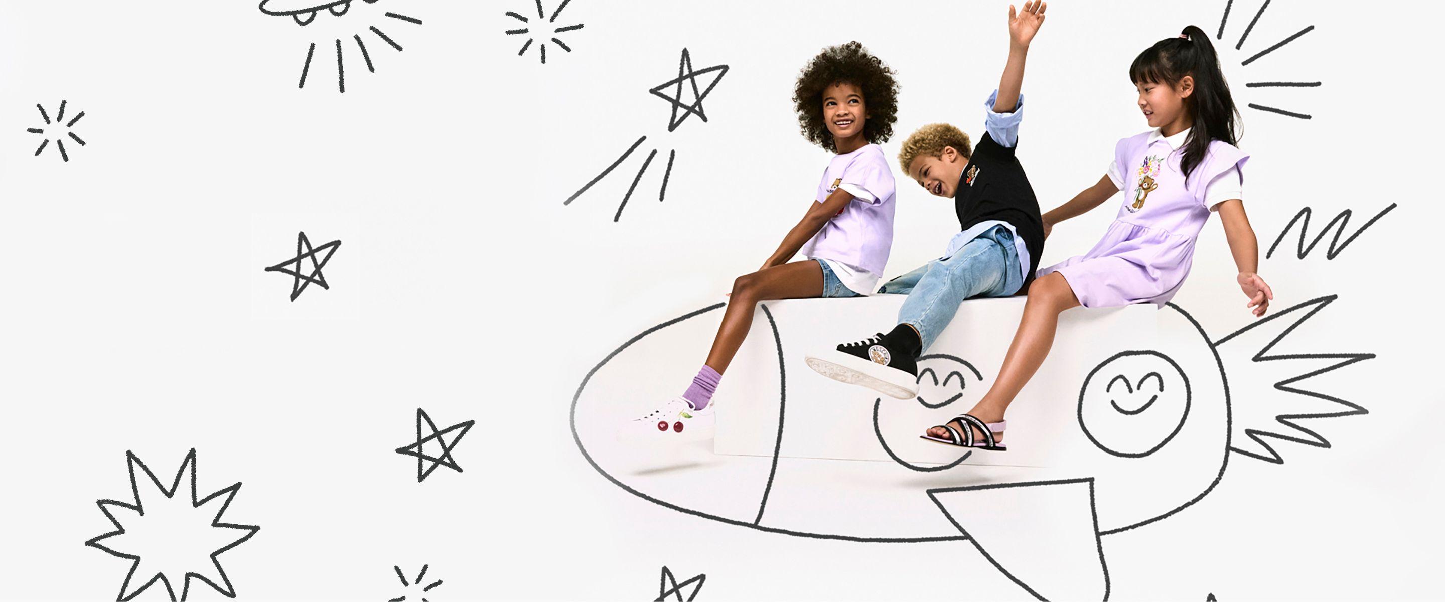 Moschino Baby Kid Teen SS26 campaign image for Scimparello Magazine featuring three children sitting on a large illustrated rocket against a white background with playful black doodle stars and space motifs. The kids wear pastel and casual summer looks, including a lilac dress with teddy bear print, light purple T-shirt with denim shorts, black T-shirt with jeans, and branded sneakers and sandals, expressing joyful movement and imaginative adventure.
