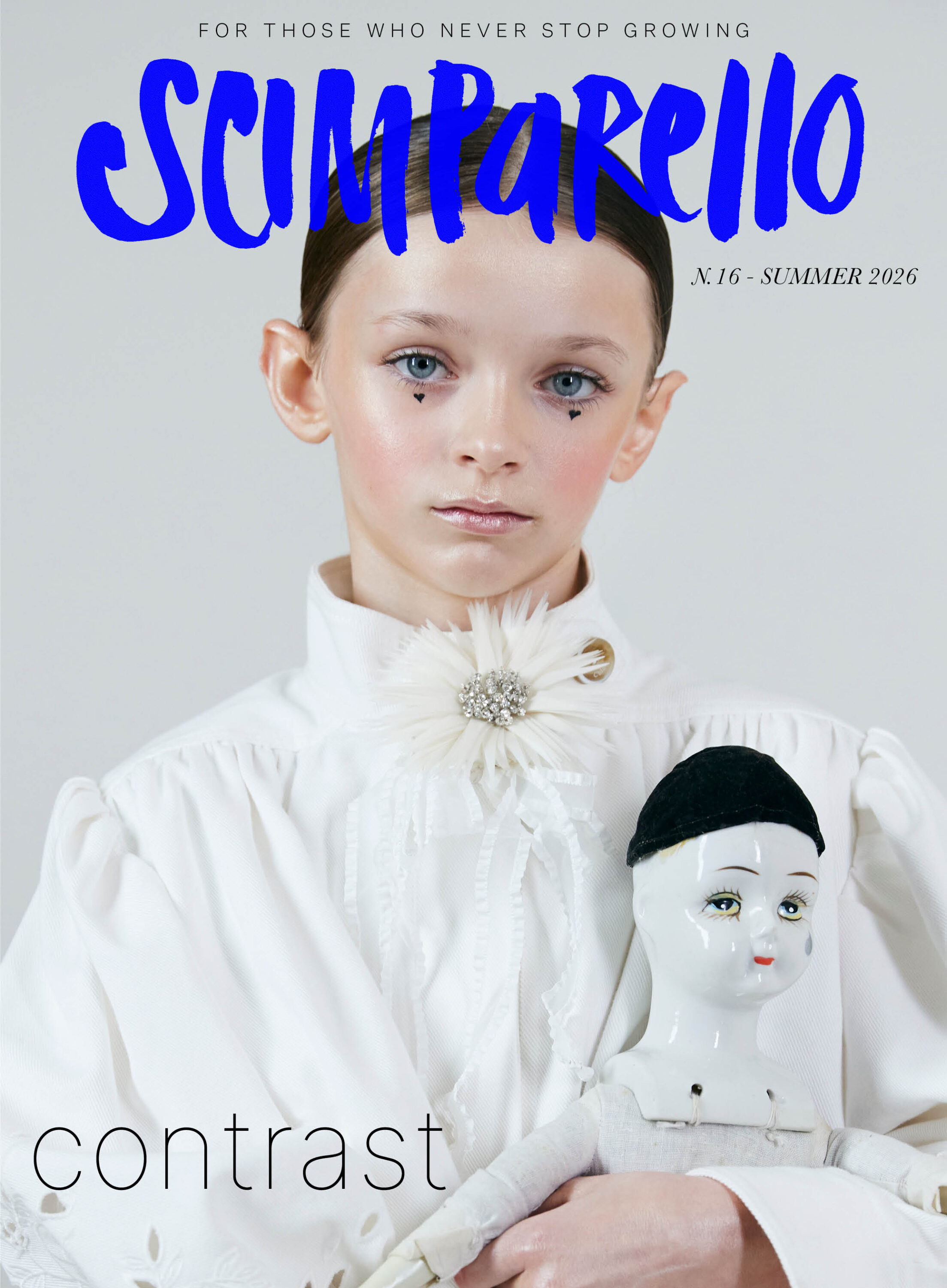Scimparello Magazine Summer 2026 issue N°16 cover featuring a young girl in a white high-neck blouse with a floral brooch, holding a porcelain doll, minimal background, soft light, blue Scimparello logo and theme contrast visible on cover