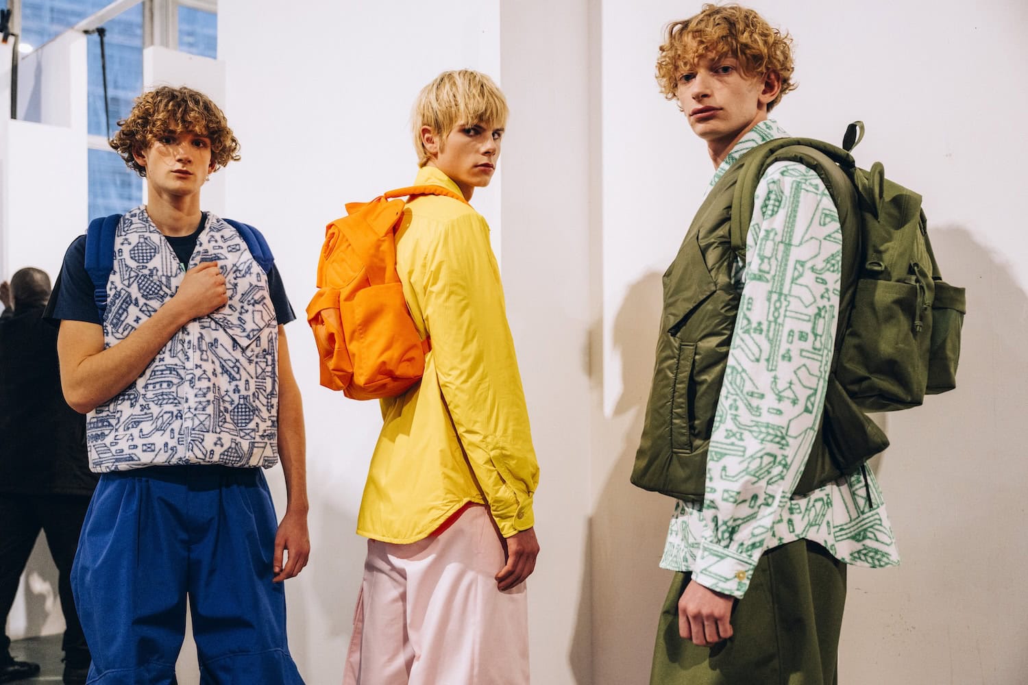 Models wearing Walter Van Beirendonck x Eastpak backpacks during Paris Fashion Week, showcasing bold colors and graphic prints in a contemporary fashion setting.
