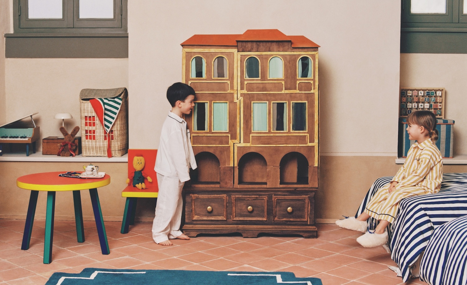 Bambini in pigiama giocano in una cameretta Zara Home x The Animals Observatory con mobile casa delle bambole, arredi rétro e dettagli colorati dal mood creativo e narrativo.