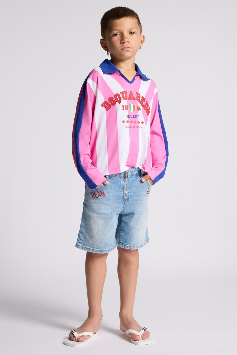 Boy wearing Dsquared2 Kids Ciao Italia capsule rugby-style pink striped top with Milano logo print, light denim shorts and white flip flops.
