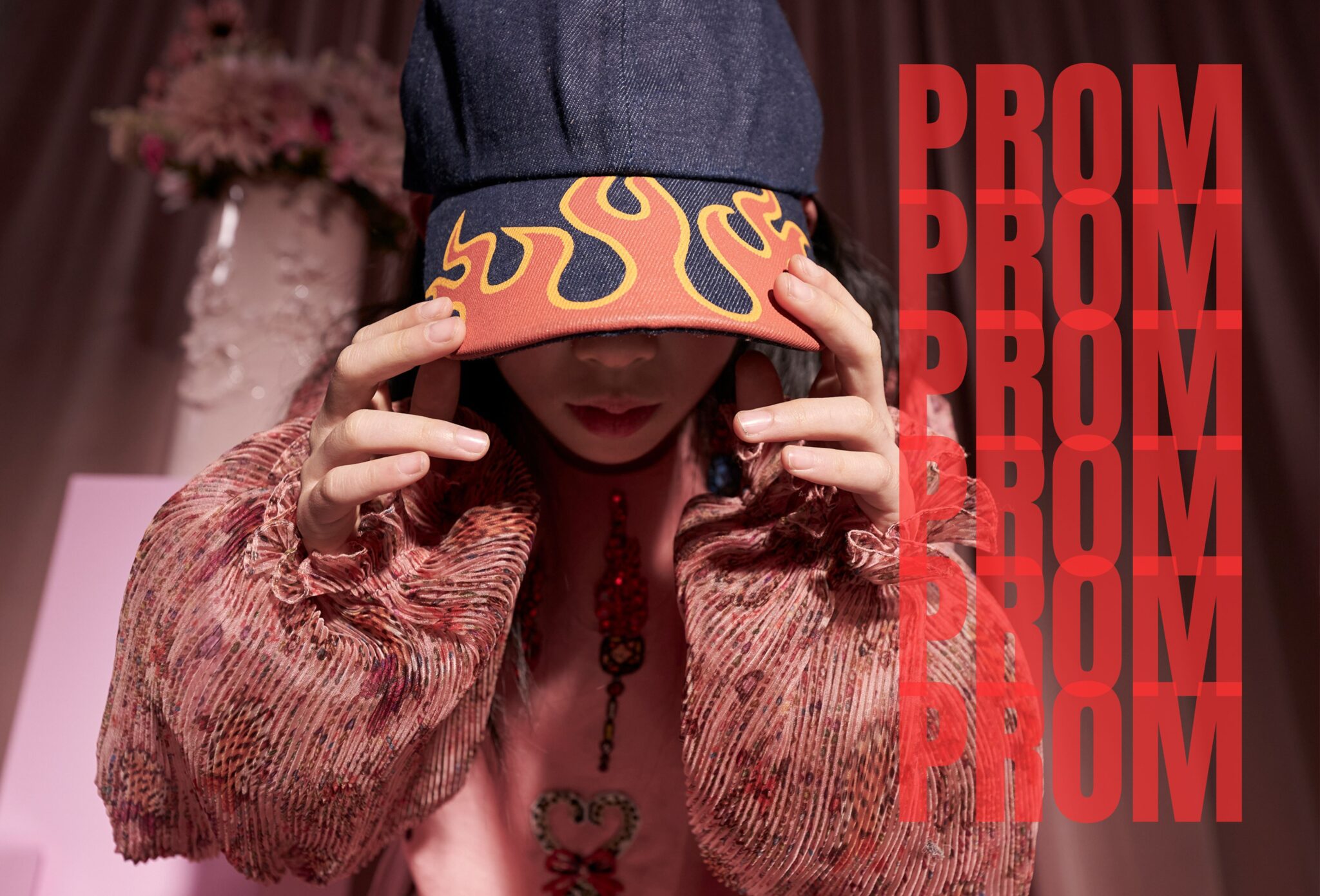 Child adjusting a navy cap with bold flame print, wearing a textured pink outfit in a studio setting with red lighting and graphic PROM text overlay. Photo by Miriam Lindthaler for Scimparello Magazine kids fashion editorial.