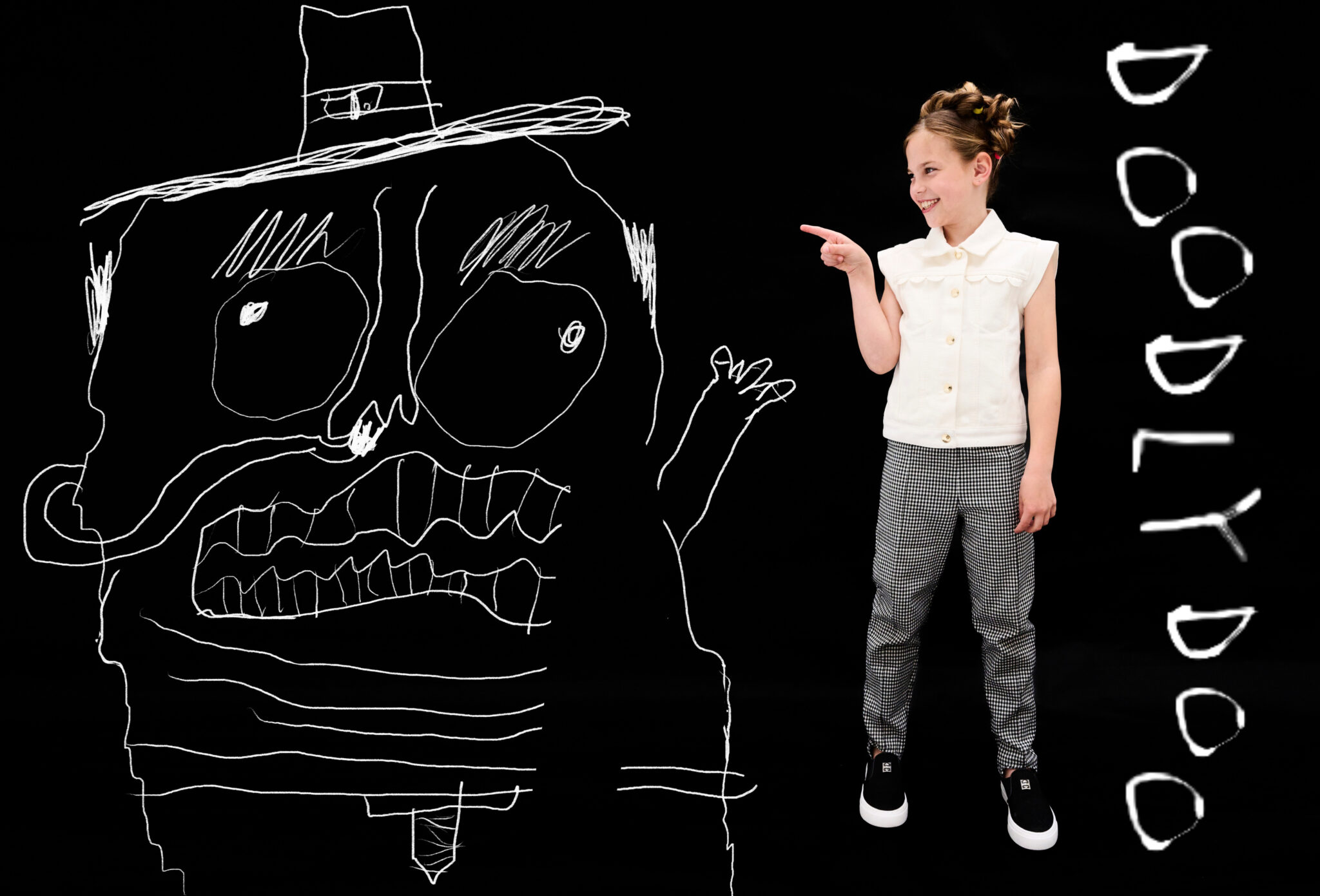 Girl in white blouse and checkered pants pointing at large hand-drawn monster with hat on black background, playful kids fashion editorial DOODLYDOO by Sophie Rata for Scimparello Magazine