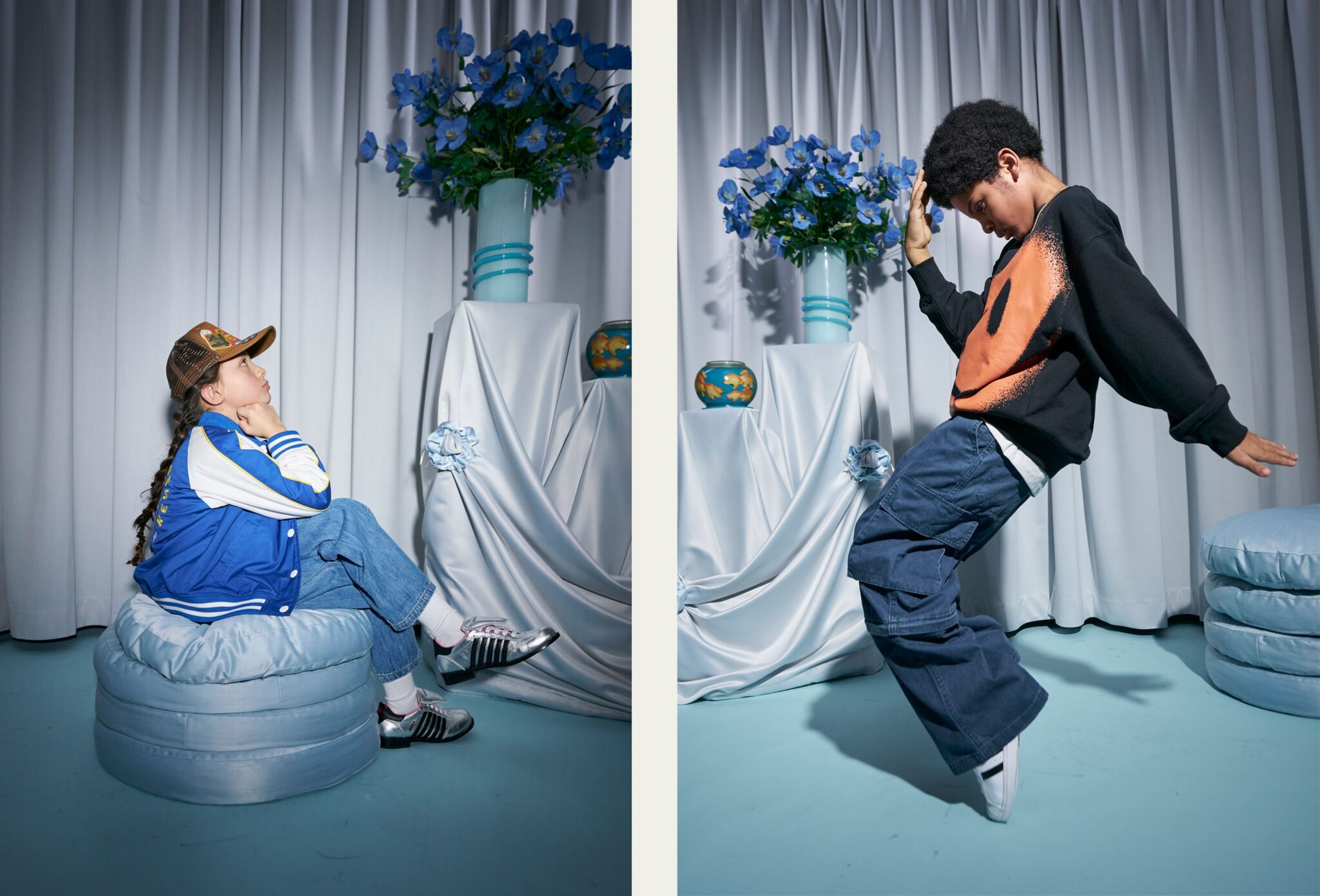 Diptych of two children styled in a studio with soft drapery and blue floral arrangements. On the left, a child in a blue varsity jacket, jeans and cap sits on a round cushion, looking upward. On the right, a child in a black sweatshirt with an orange graphic and wide-leg pants strikes a dynamic pose mid-movement. Photo by Miriam Lindthaler for Scimparello Magazine kids fashion editorial PROM.