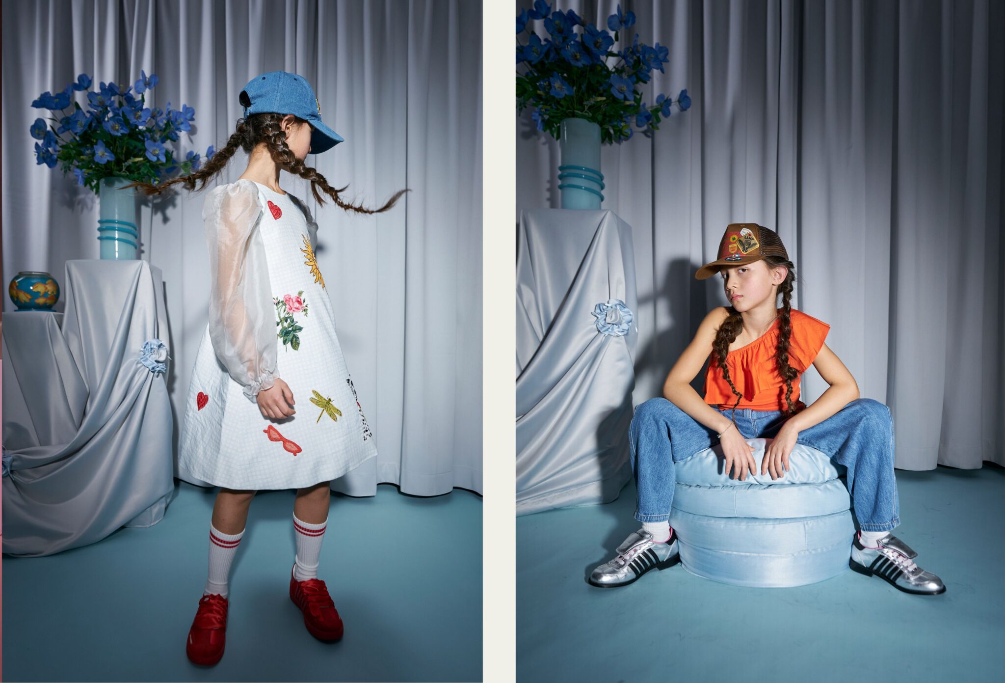 Diptych of two children in a studio setting with soft drapery and blue floral arrangements. On the left, a child in a white dress with embroidered motifs and sheer sleeves turns with braided hair and a blue cap. On the right, a child in an orange top, jeans and a brown cap sits casually on a round cushion, wearing silver sneakers. Photo by Miriam Lindthaler for Scimparello Magazine kids fashion editorial PROM.