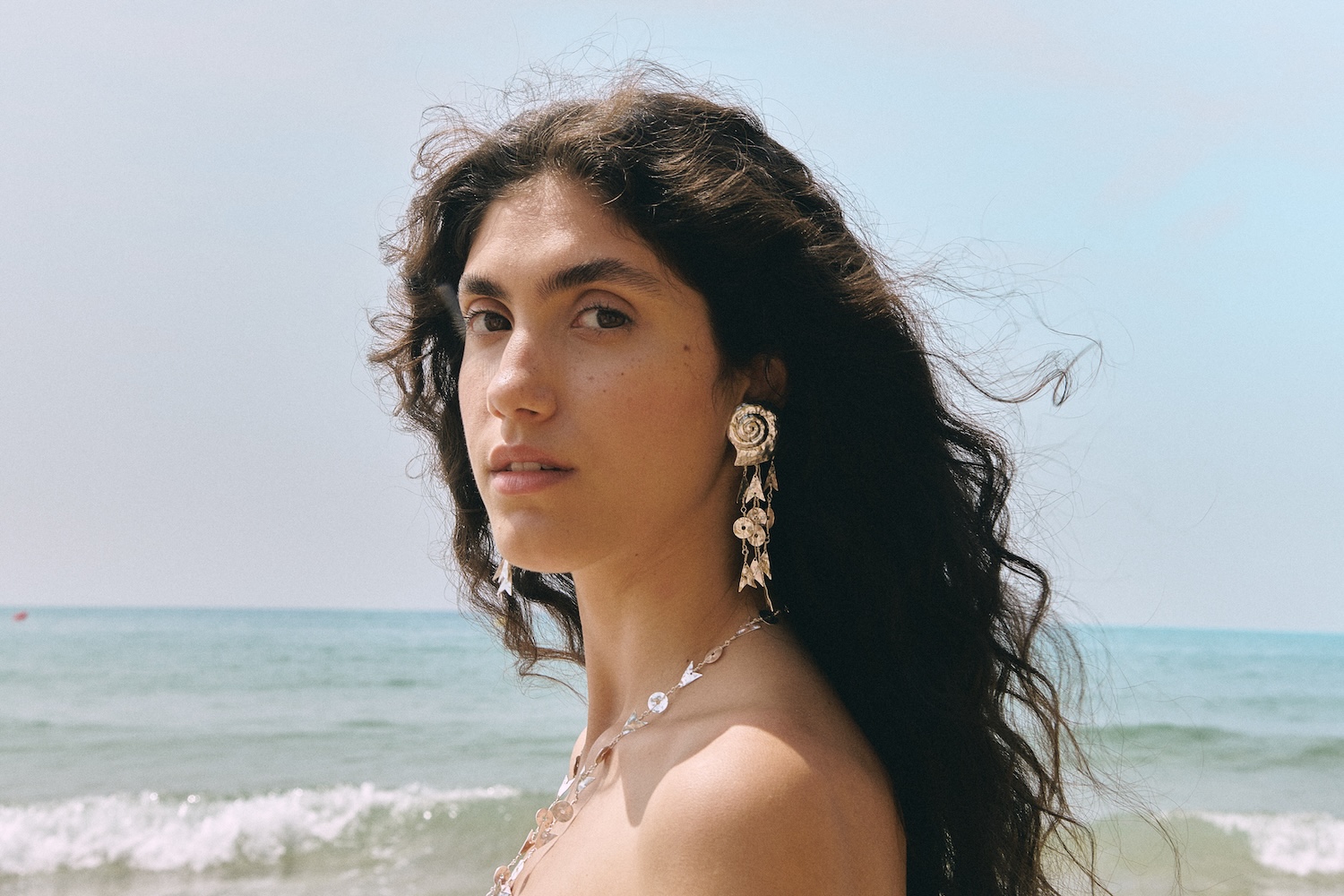 Woman wearing statement shell earrings and necklace by the sea, showcasing handcrafted jewelry inspired by Andalusian coastal culture