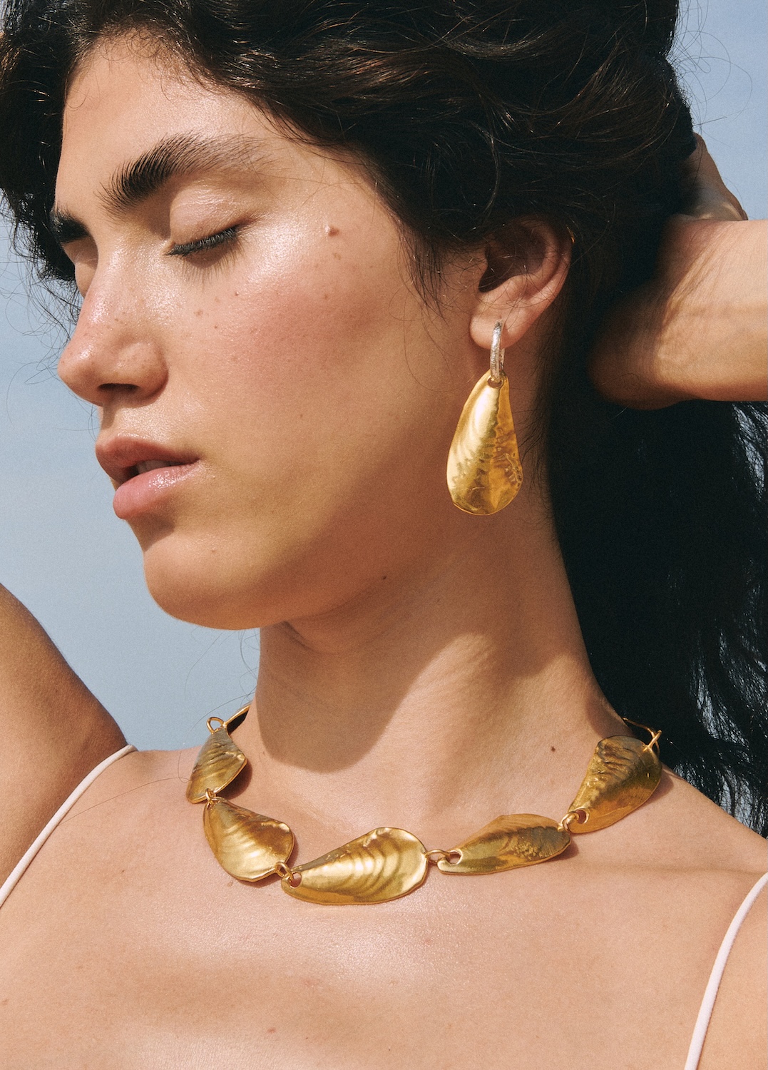 Close-up of woman wearing gold statement necklace and earrings with organic shapes, inspired by seashells and natural elements