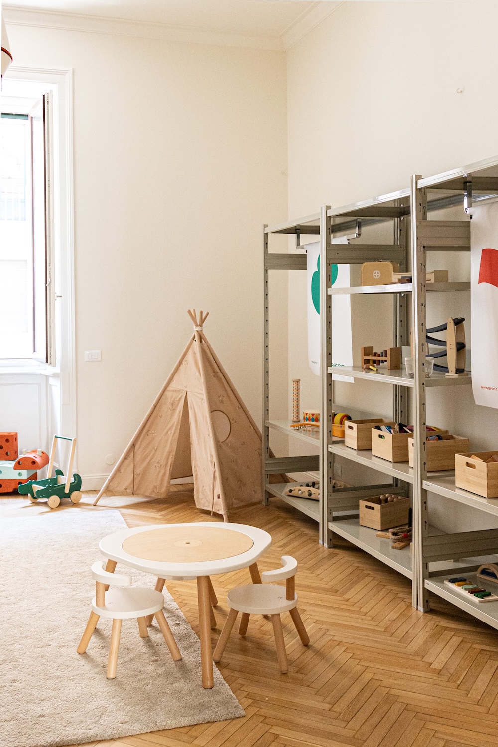 Kids playroom interior at Young Folks Milan Design Week featuring wooden toys, modular shelving, teepee tent and round child-sized table and chairs