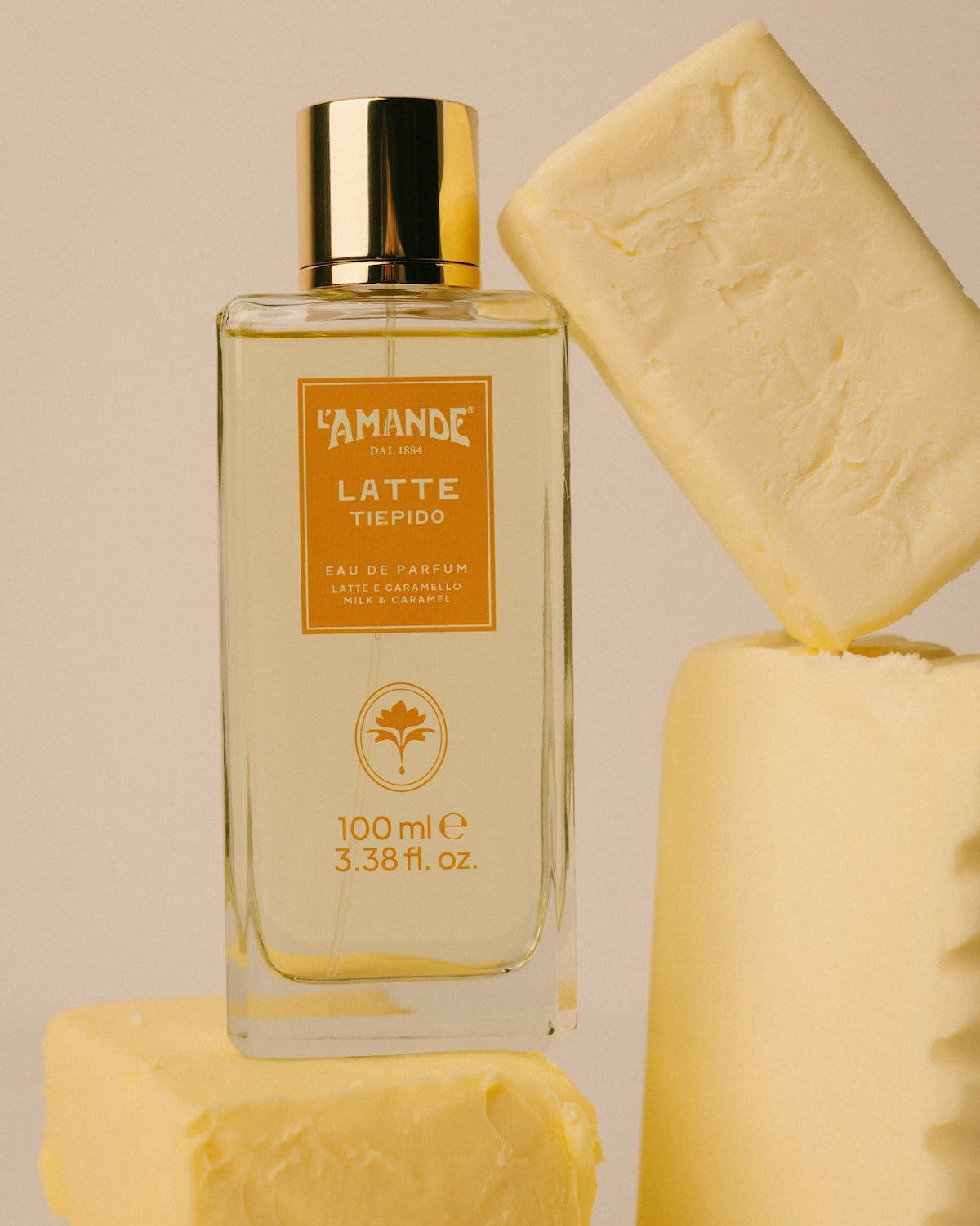 L’Amande Latte Tiepido eau de parfum bottle with milk and caramel scent, styled with artisanal soap blocks on a warm neutral background.