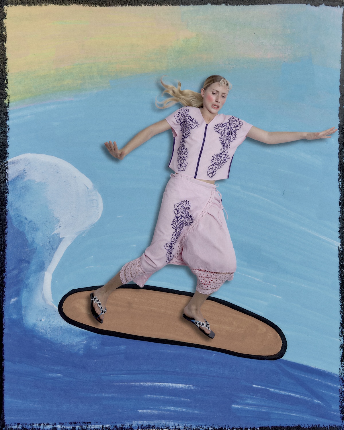 Woman in a soft pink embroidered co-ord surfing on a painted wave, wearing floral sandals, combining relaxed resortwear with a dreamy, playful aesthetic.
