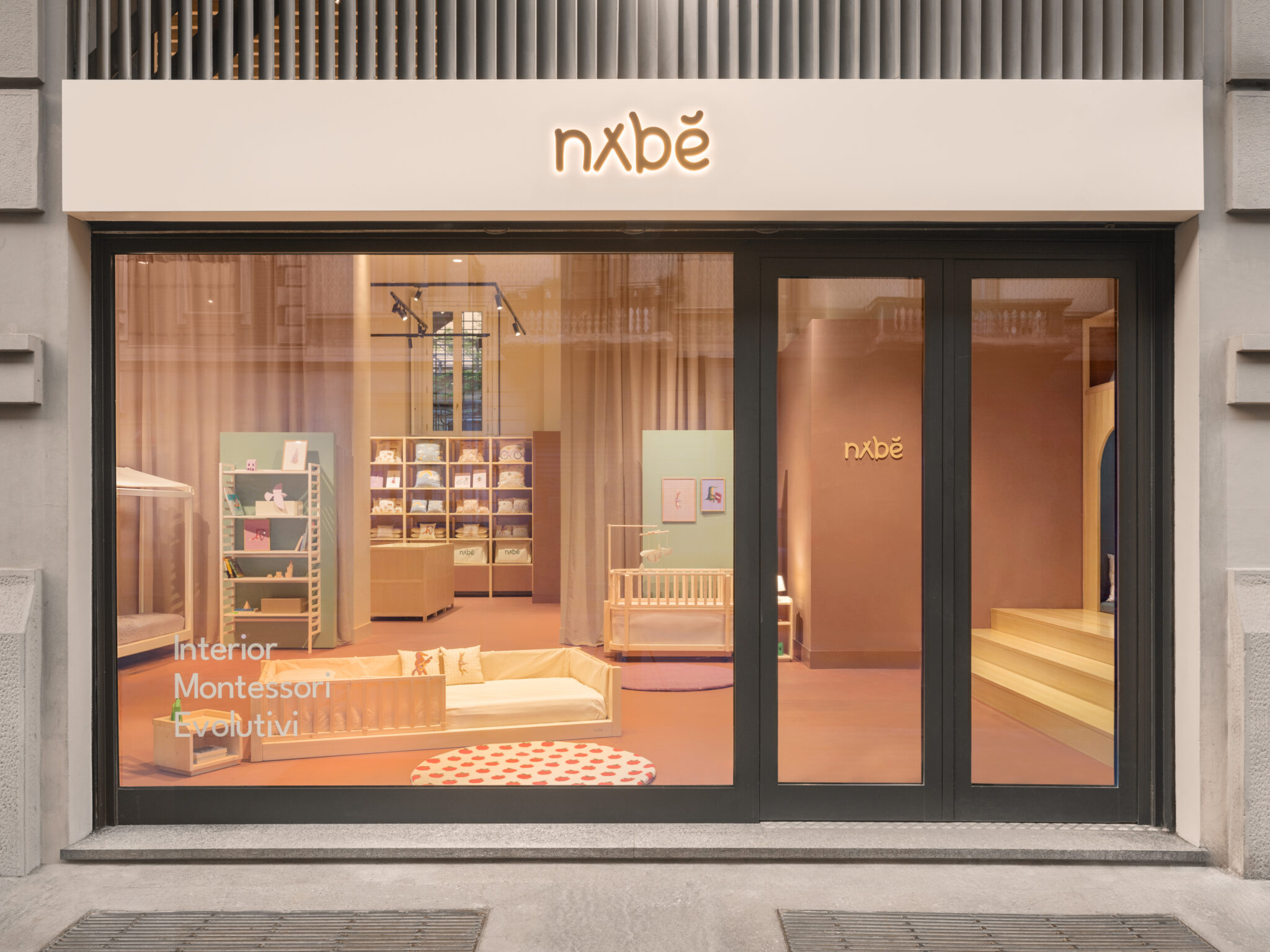 Nabè flagship store in Milan showcasing Montessori-inspired kids furniture with soft pastel interiors, low wooden bed, crib and modular shelving visible through storefront window