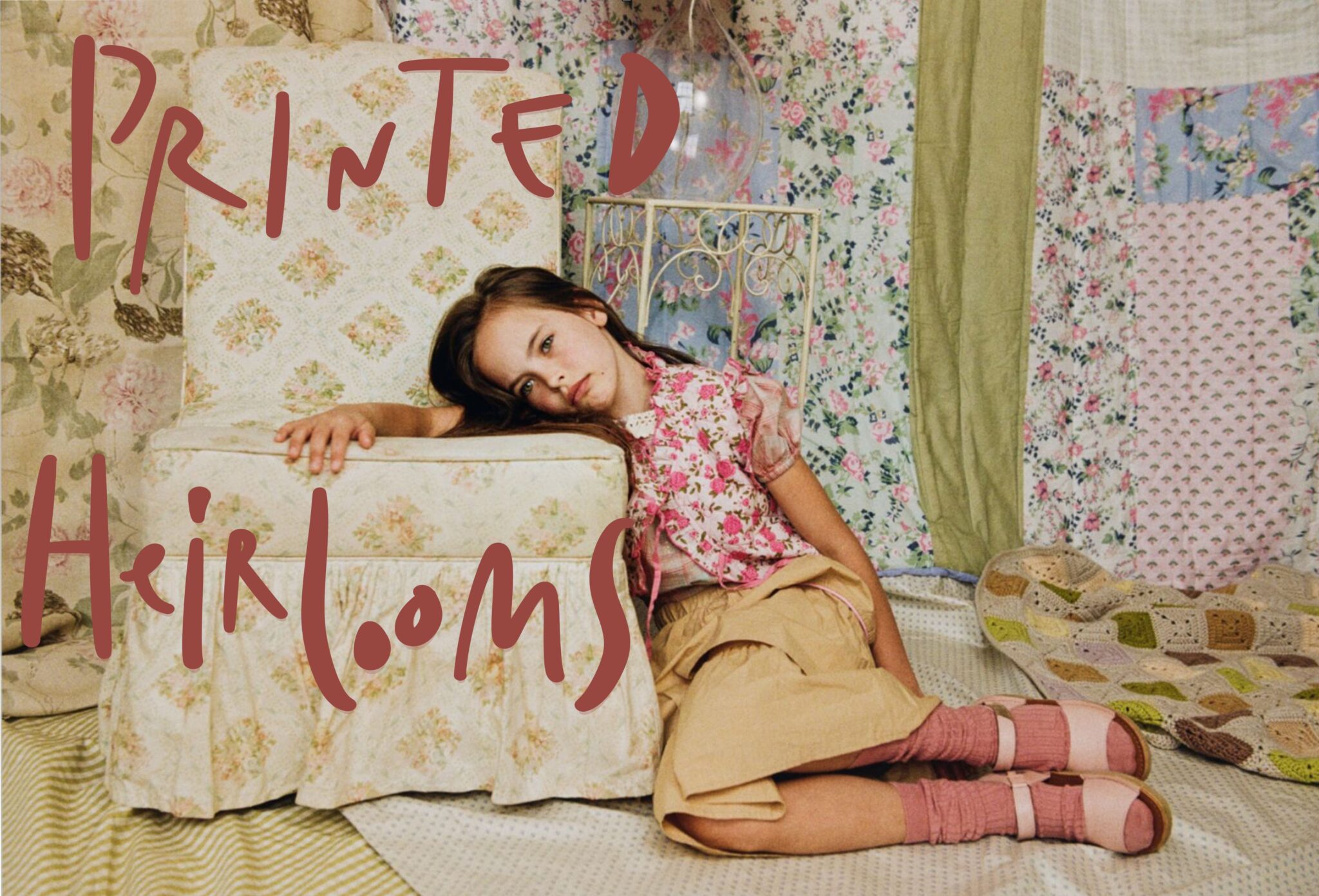 Young girl in a floral kids fashion look sits beside a vintage floral armchair in a room filled with layered printed fabrics, crochet details and soft nostalgic colors for Scimparello Magazine editorial Printed Heirlooms by Emma Wright.